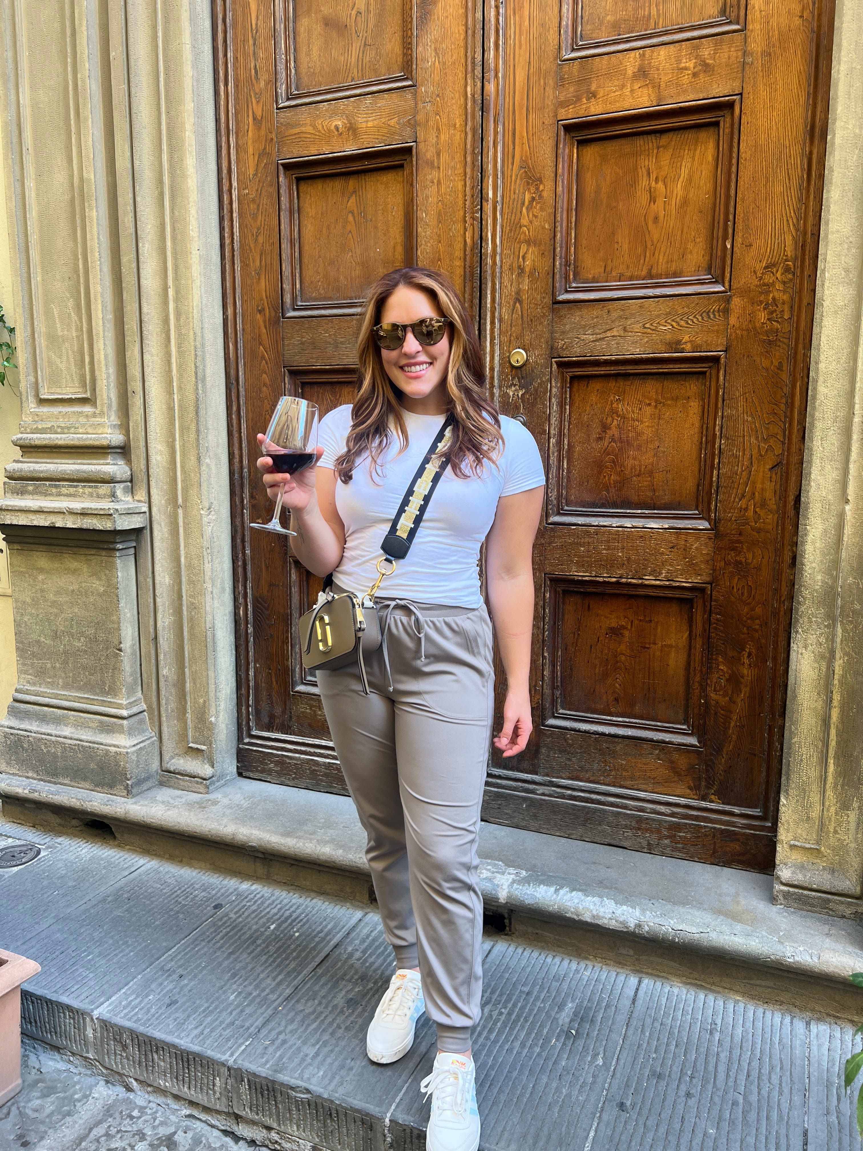 Leah standing in front of a large wooden doorway, holding a glass of red wine. 