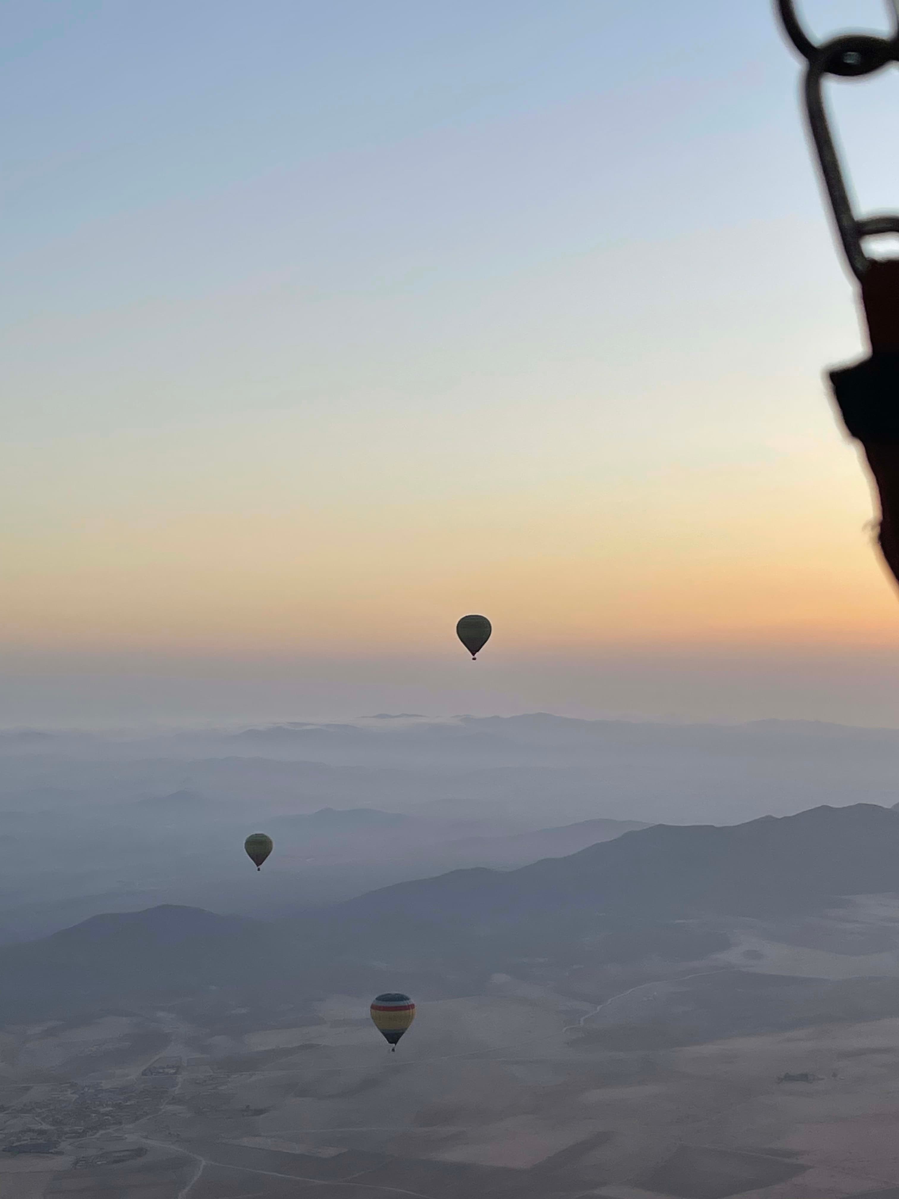 Beautiful view of three hot air balloons floating as the sun rises over mountains