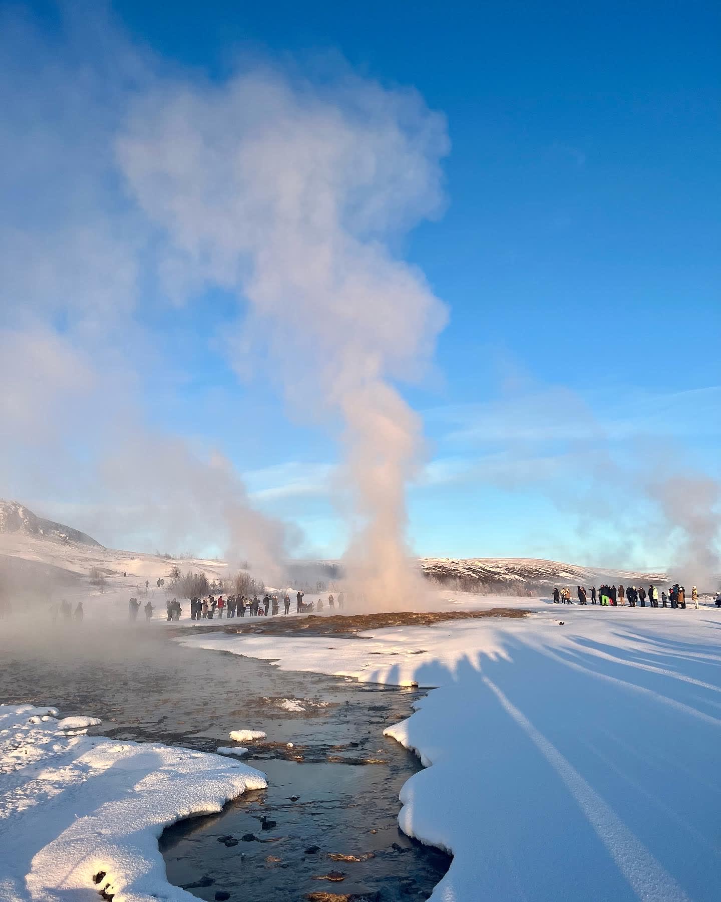 Beautiful view of steam coming from Strokkur Geyser surrounded by snow on a clear day