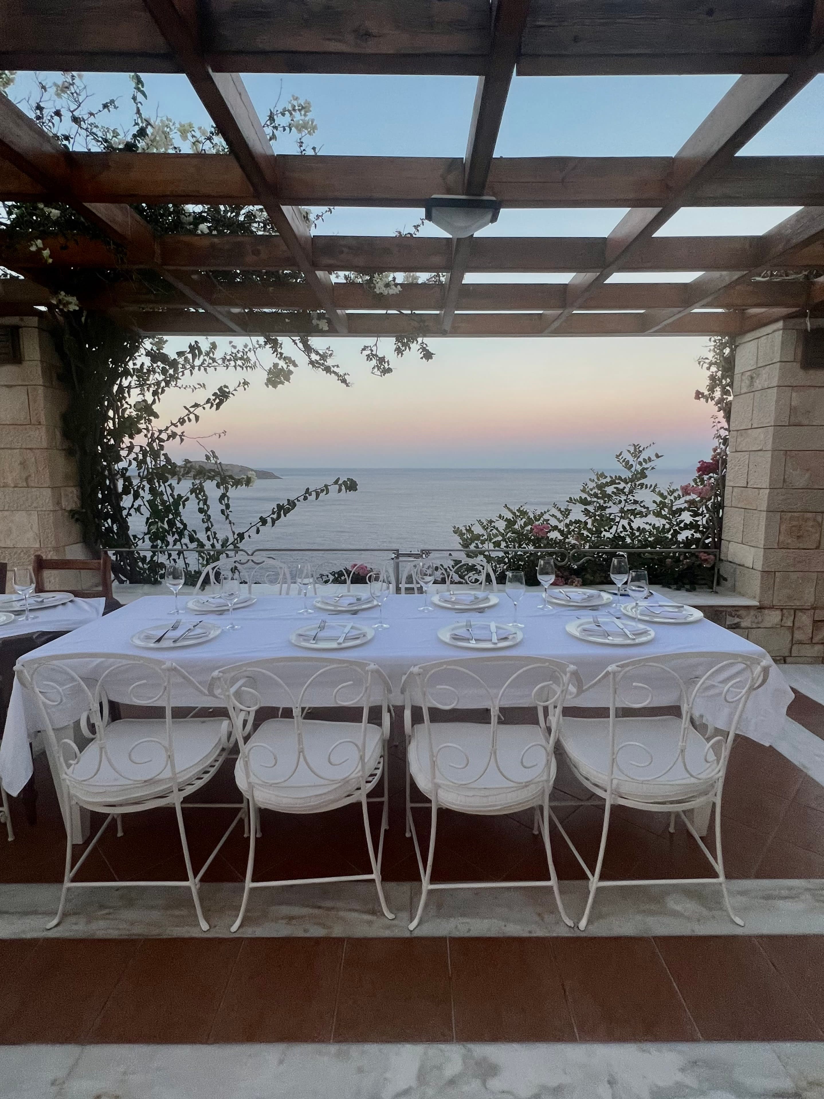 Photo of a white cloth dinner table set with plates and featuring beautiful views of the ocean in the distance