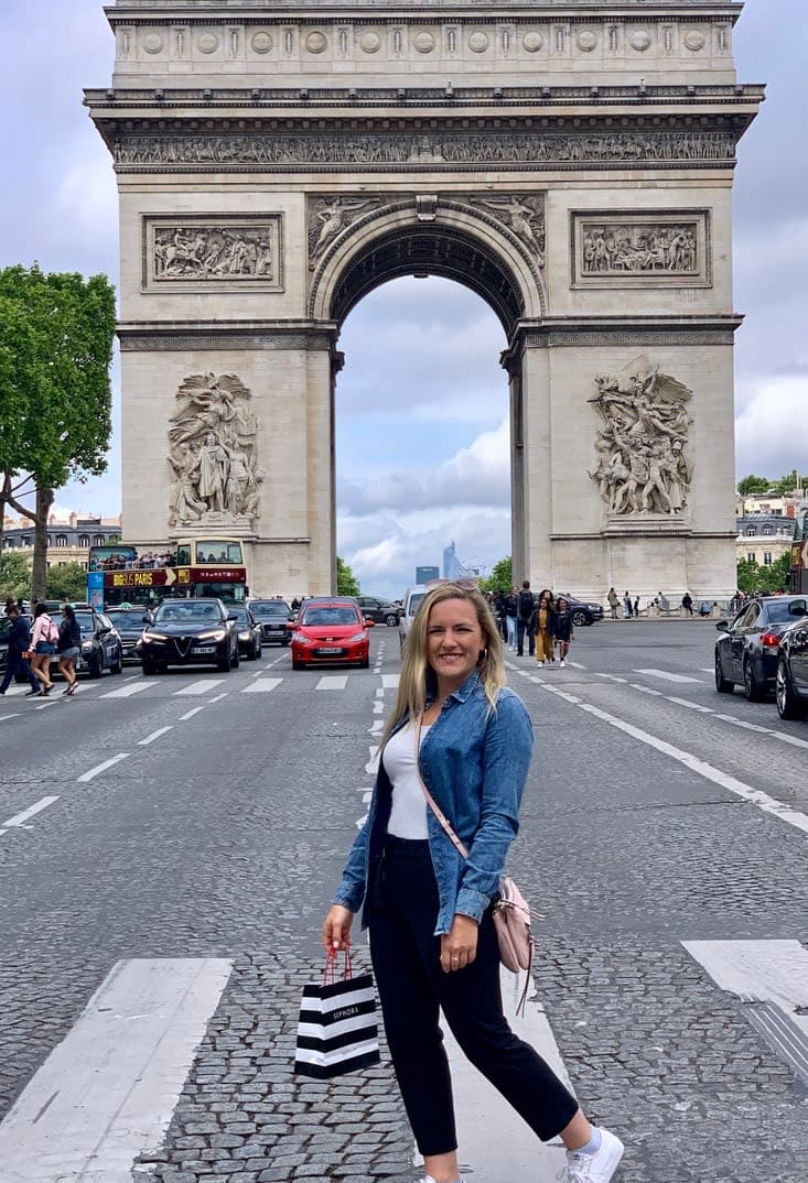 Olivia holding a bag and posing on the street with the Arc de Triomphe monument in the background
