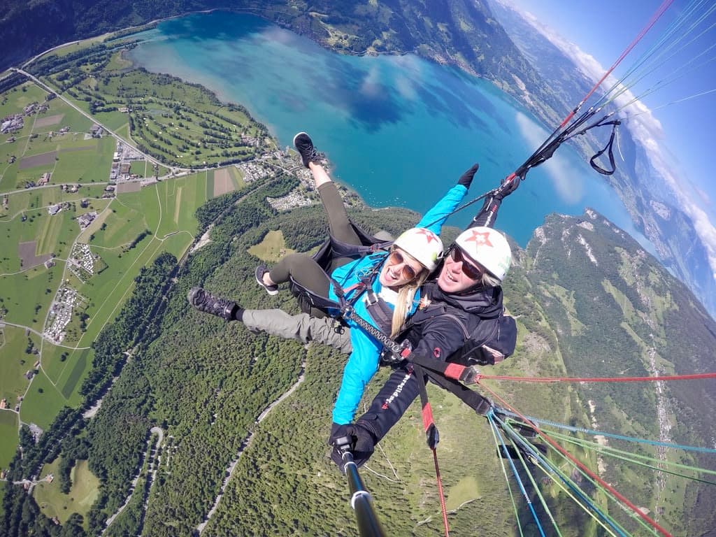 Olivia wearing a blue jacket and helmet paragliding above a beautiful coastal landscape on a clear day