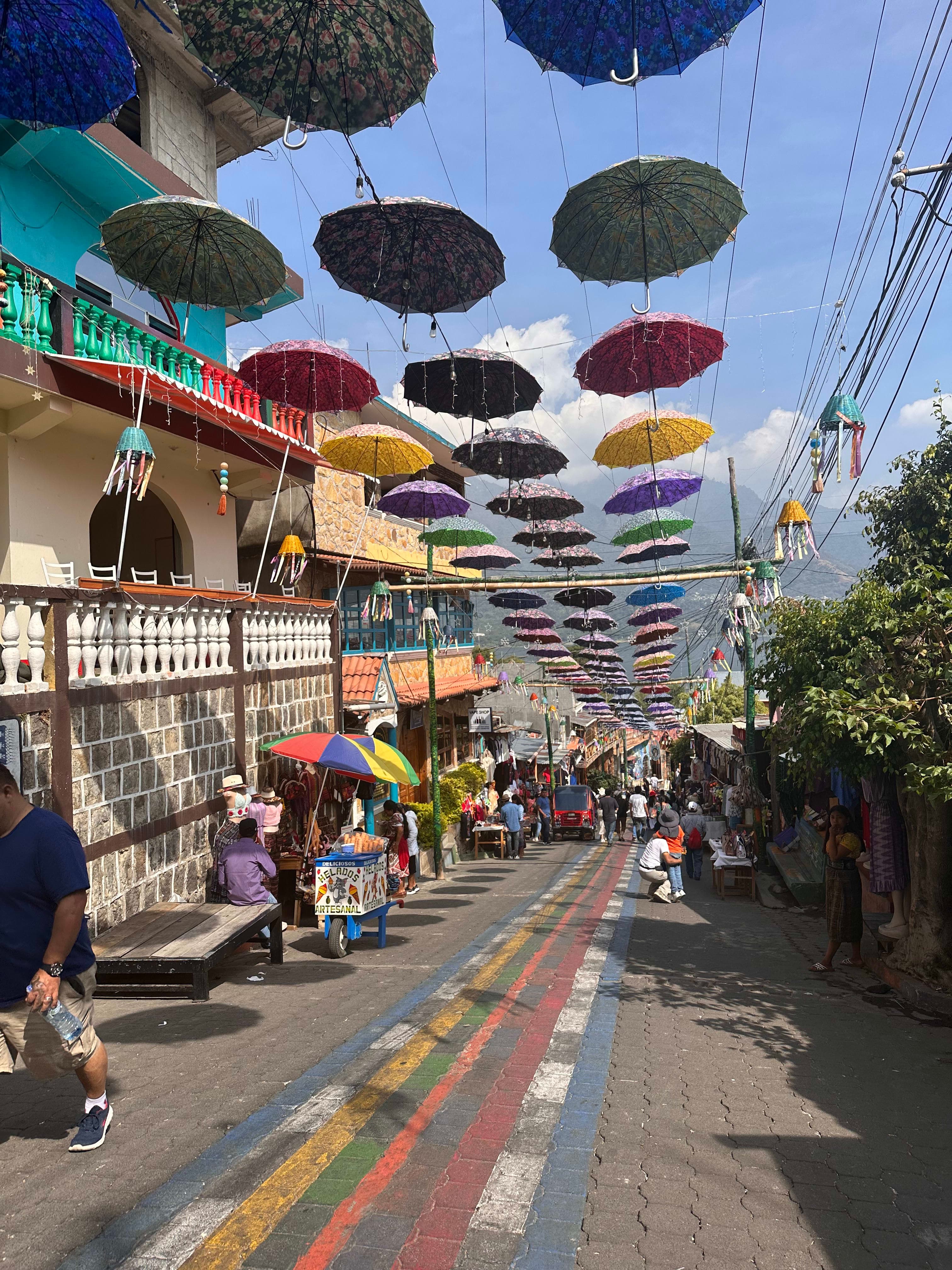 View of an empty street with colorful umbrellas hanging above on a sunny day