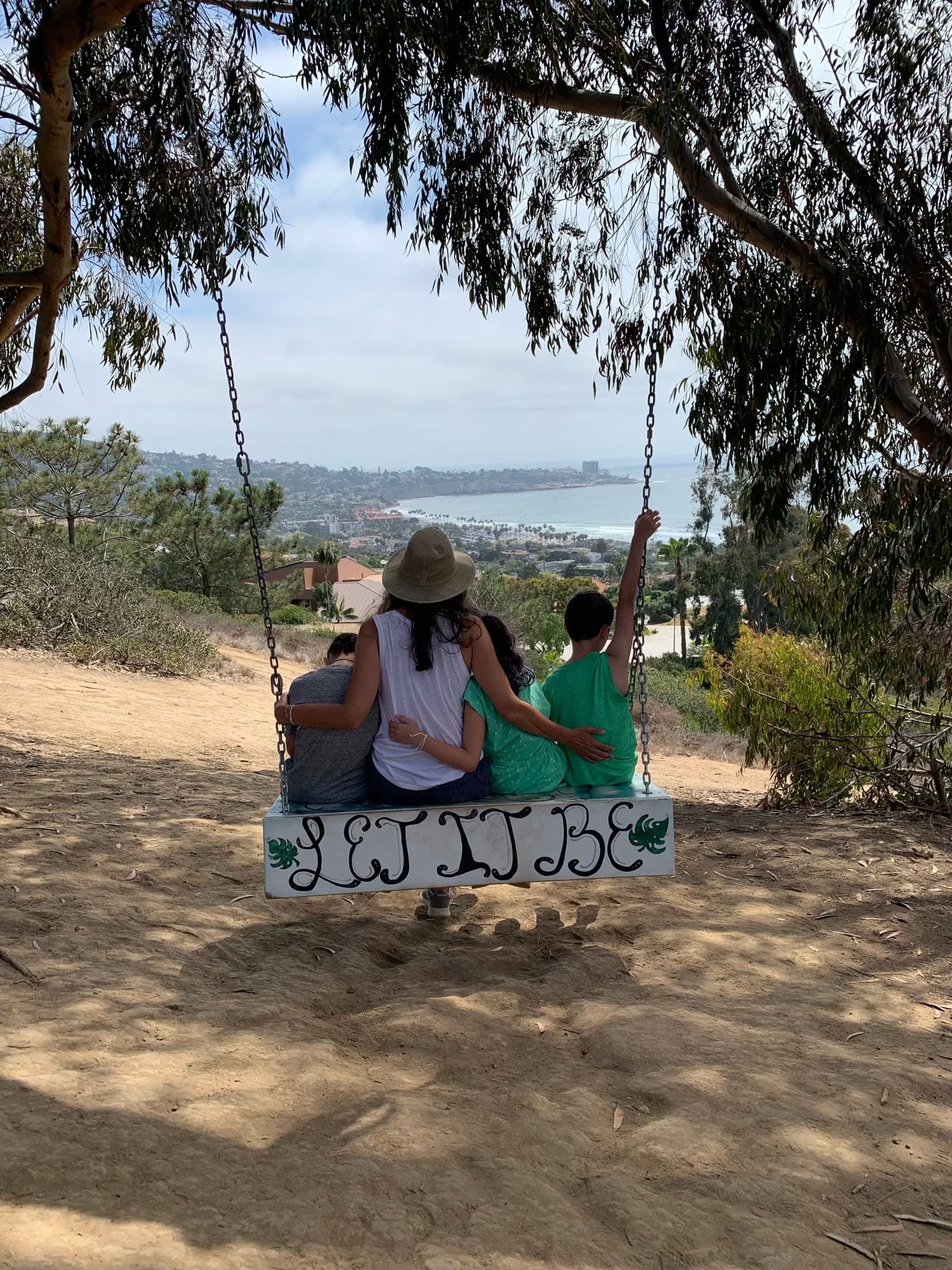 Advisor and children sitting on a swing reading “let it be” with a view of the coast in the distance