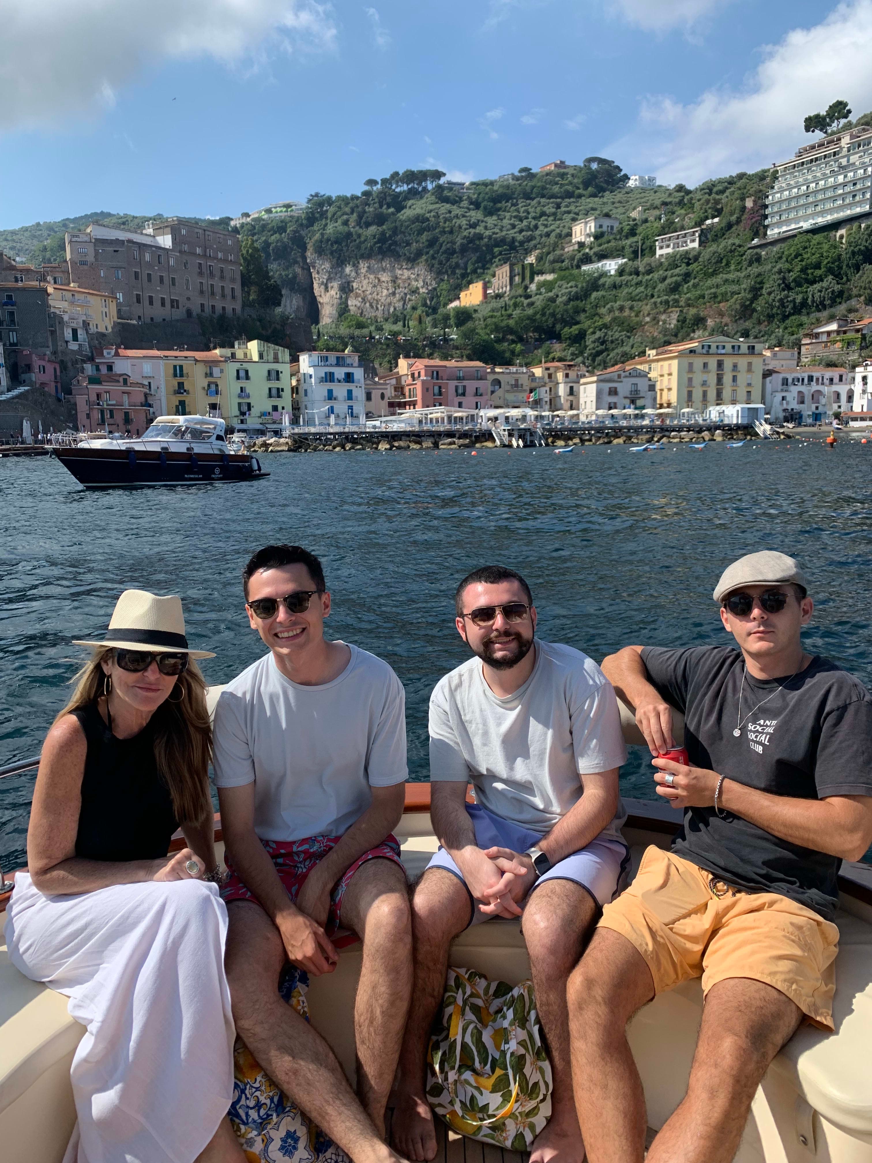 Advisor and fellow travelers posing on a boat facing the coast on a sunny day. 