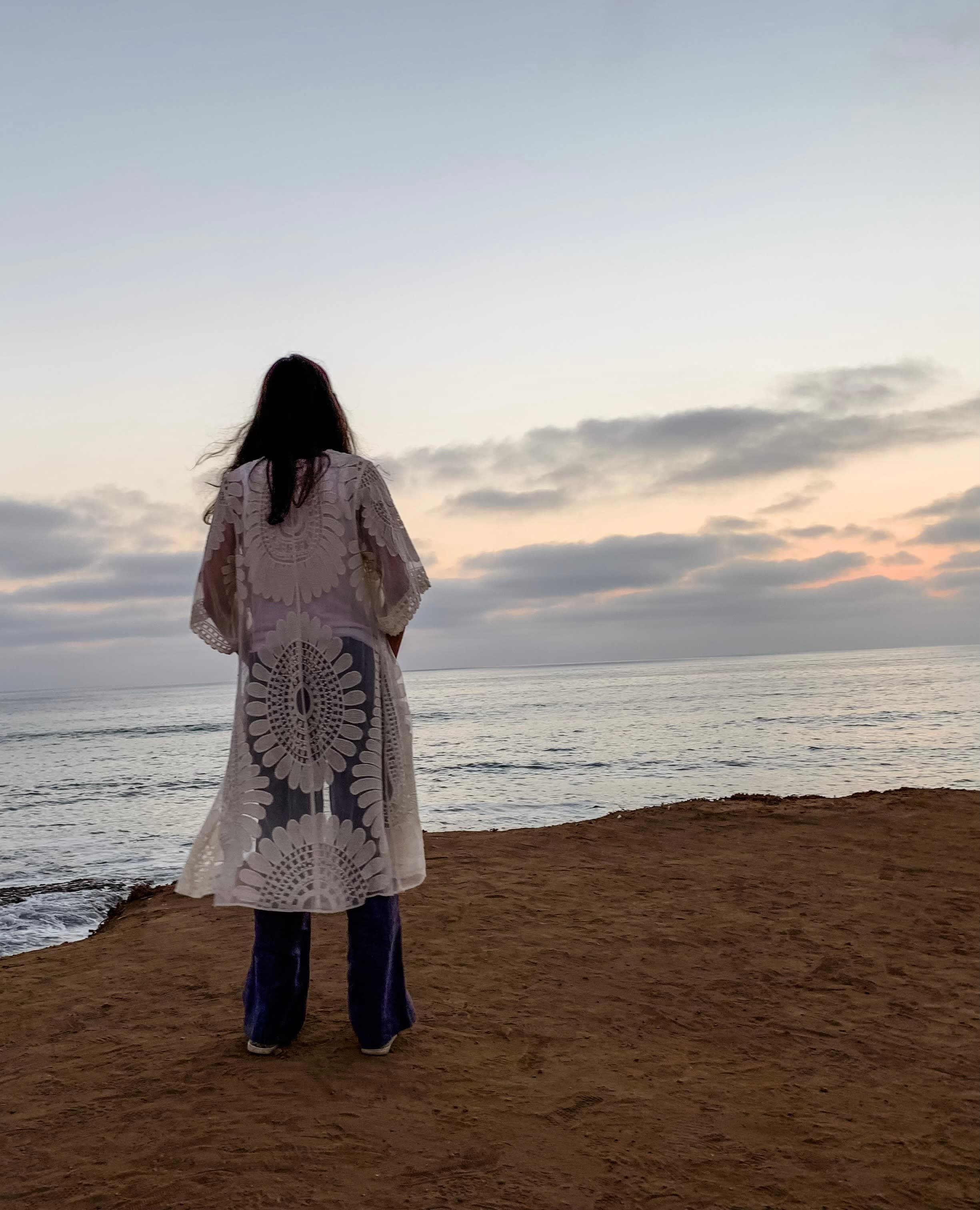 Advisor standing on the beach in a long white robe at sunset