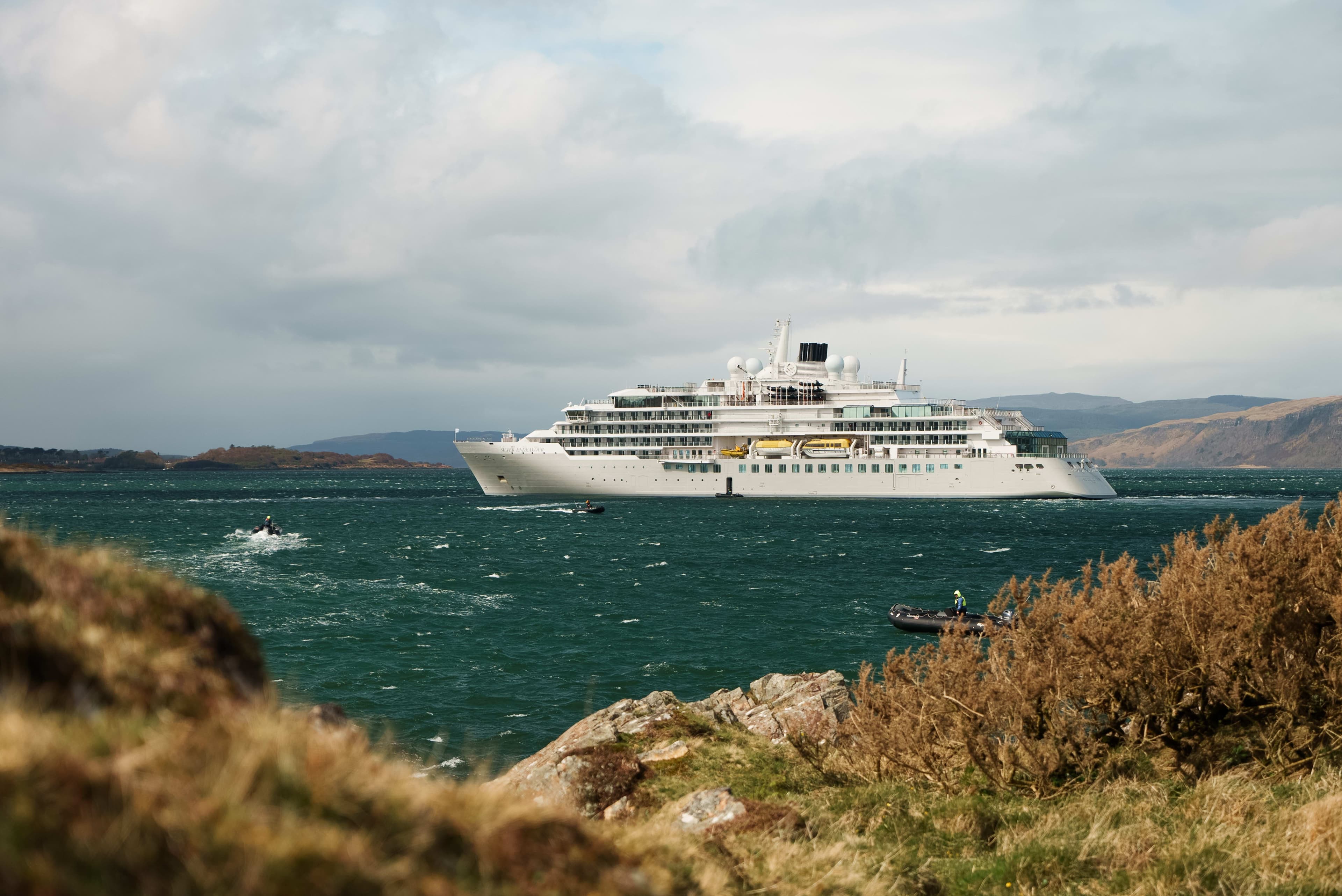 a cruise ship in choppy ocean waters off the coast with clouds during day