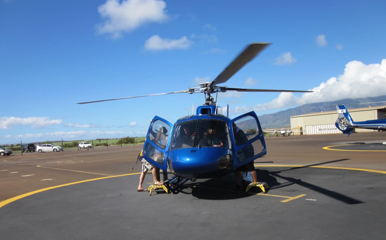 A picture of a blue helicopter on a helipad with people climbing aboard.