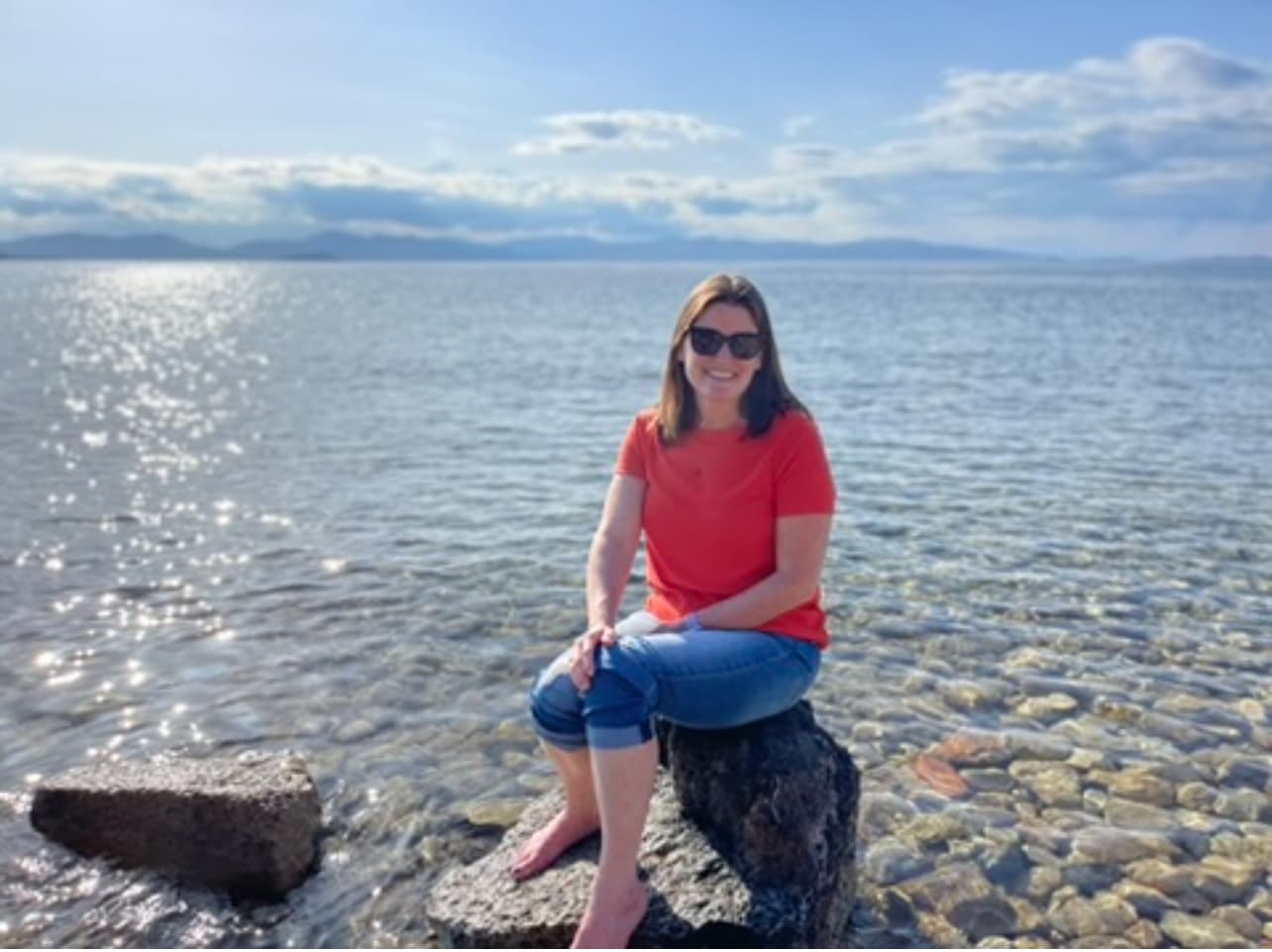 Travel advisor Erin sitting on a rock surrounded by a shallow water body on a sunny day
