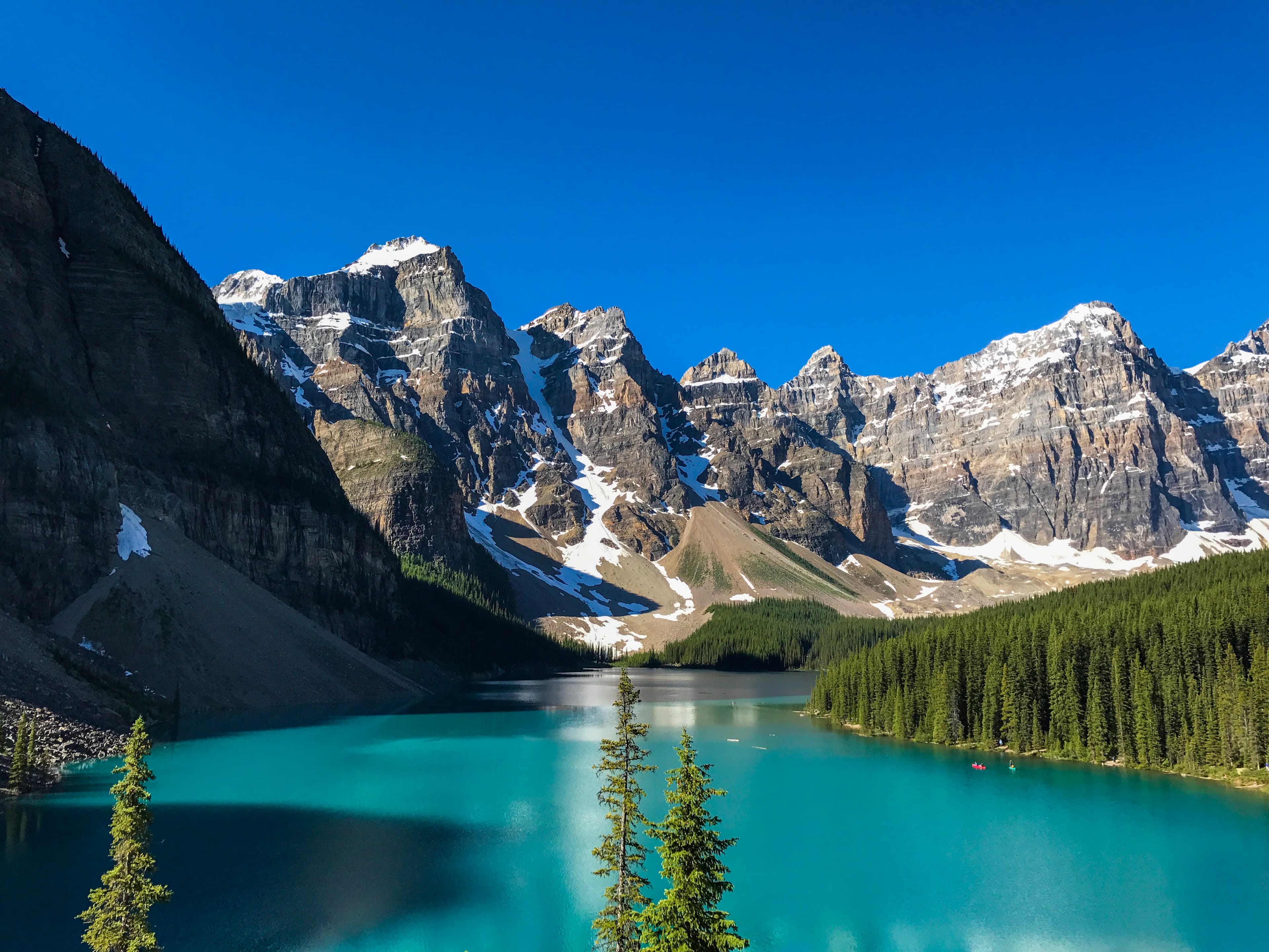 A beautiful view of a turquoise body of water with snow-capped mountains and greenery around