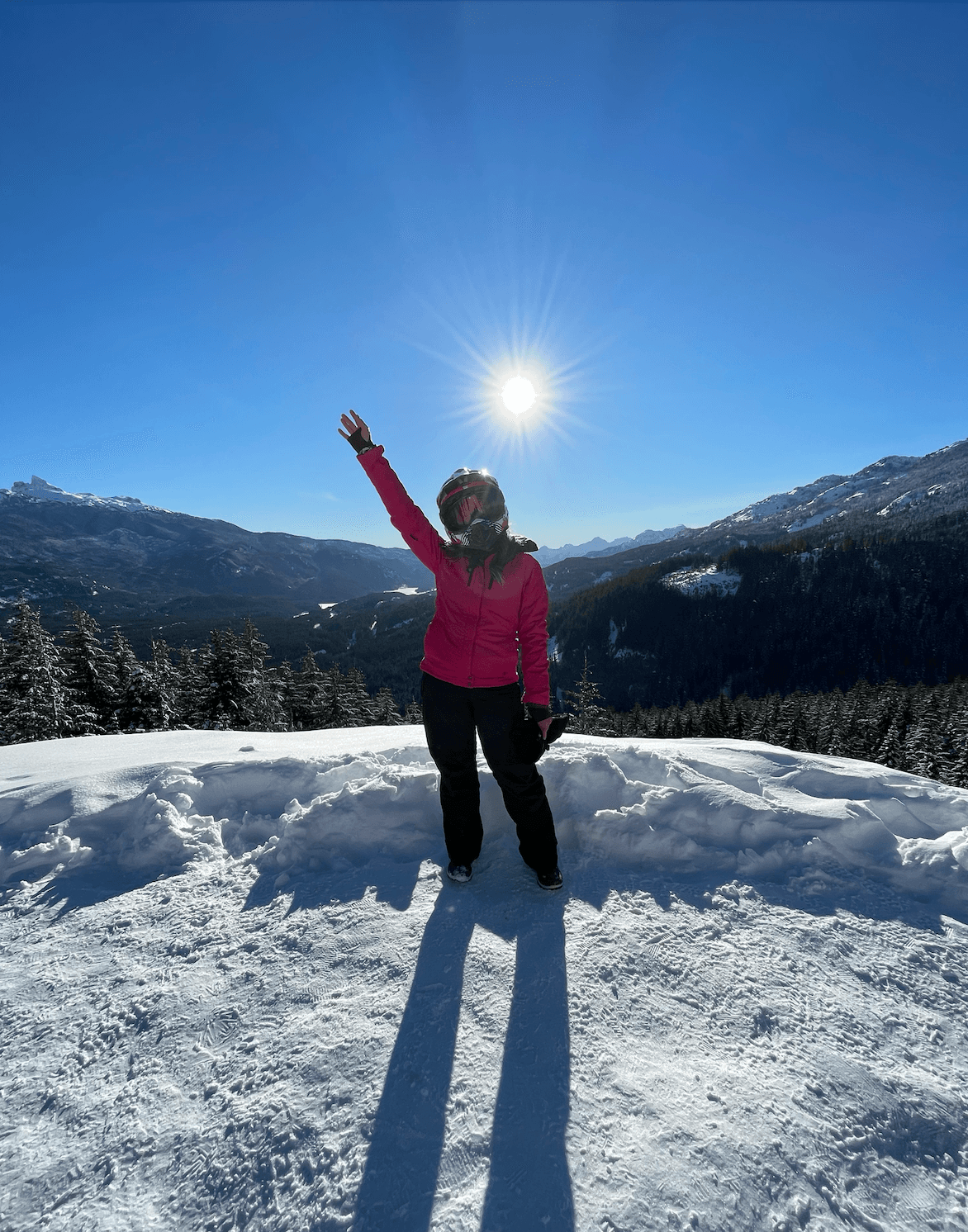 Picture of Sofia wearing winter gear and posing at the top of a snowy mountain under a bright sun