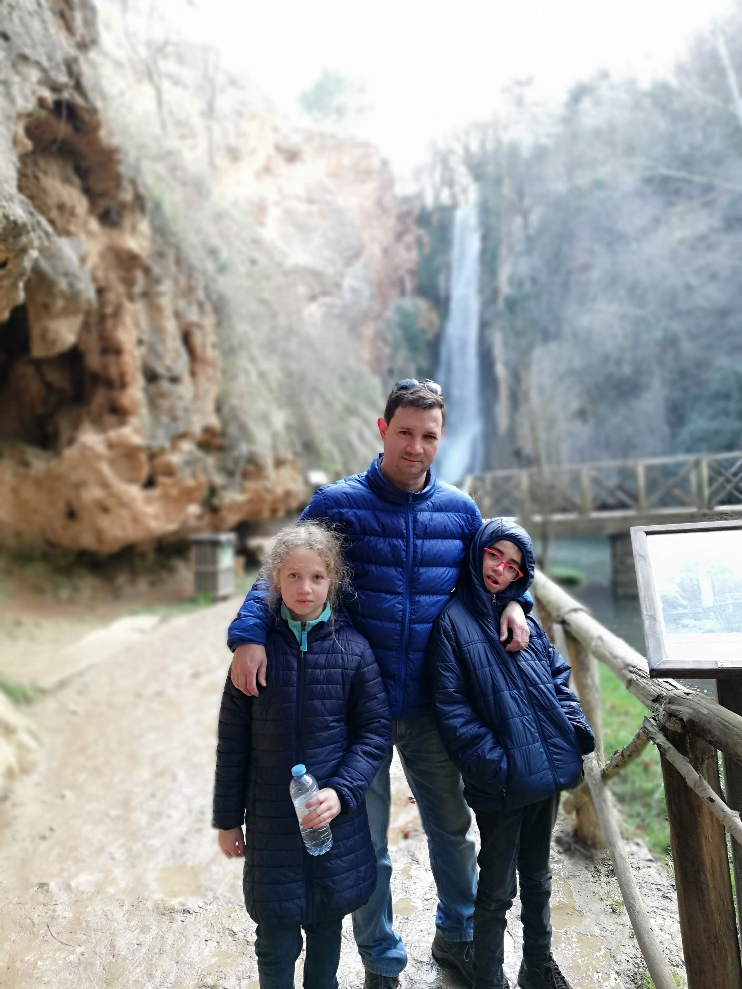 Advisor posing with his children at a waterfall in the daytime.