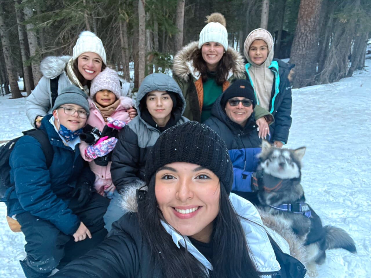 Advisor posing with a group of people in a snow covered region with a forest in the distance. 