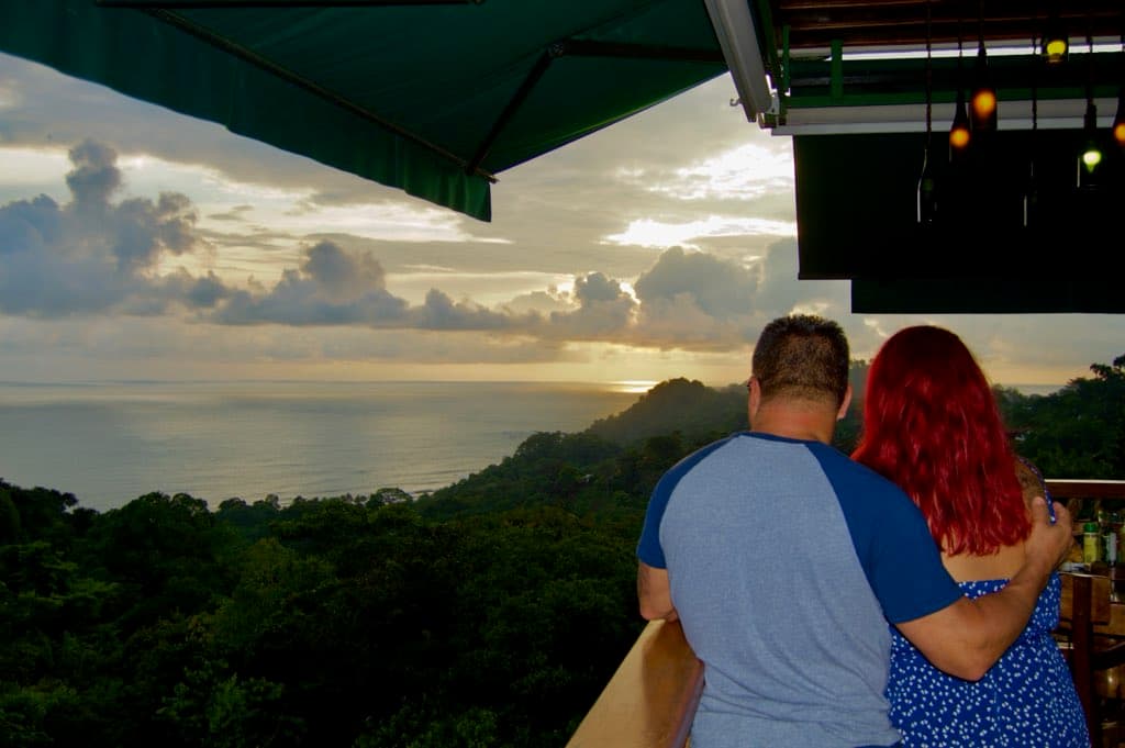 Advisor posing with her husband looking at a beautiful sunset over a jungle with the ocean in the distance. 