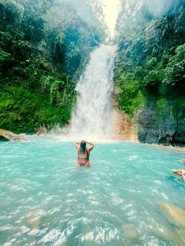 Advisor swimming in a body of water with a waterfall in the distance on a sunny day. 