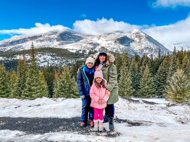 Advisor posing with her family in a snow covered region with mountains in the distance and a forest. 
