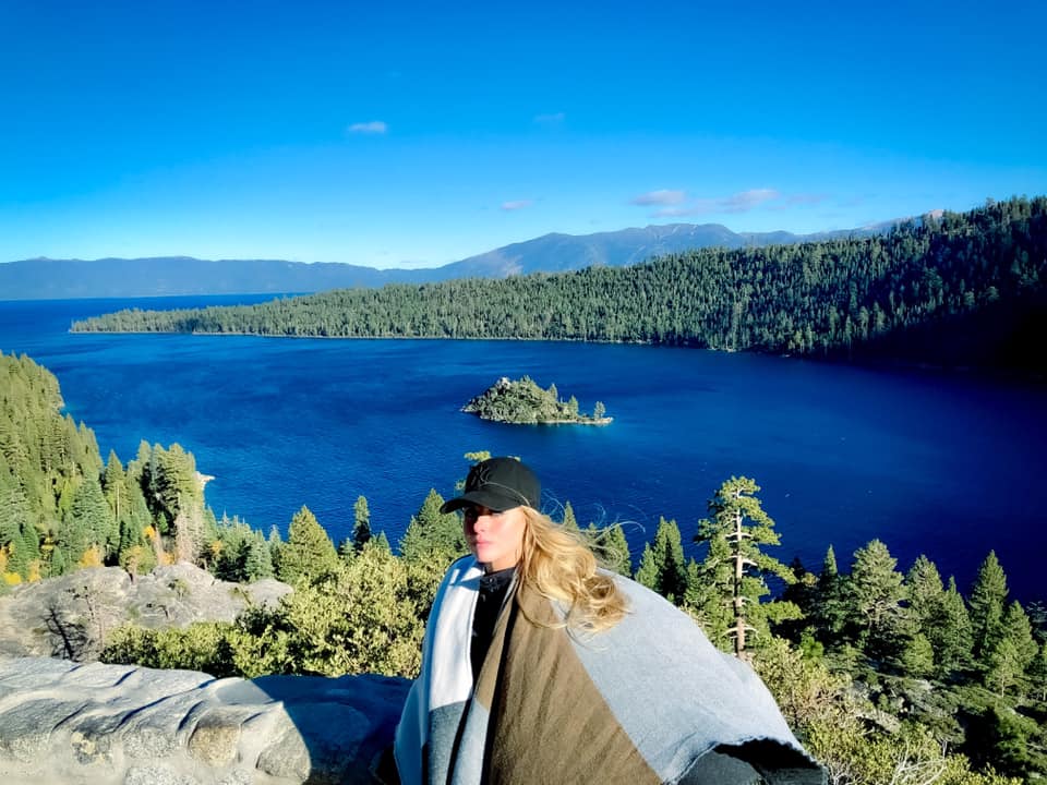 Advisor posing on a lookout point with a body of water, mountains and a forest in the distance. 