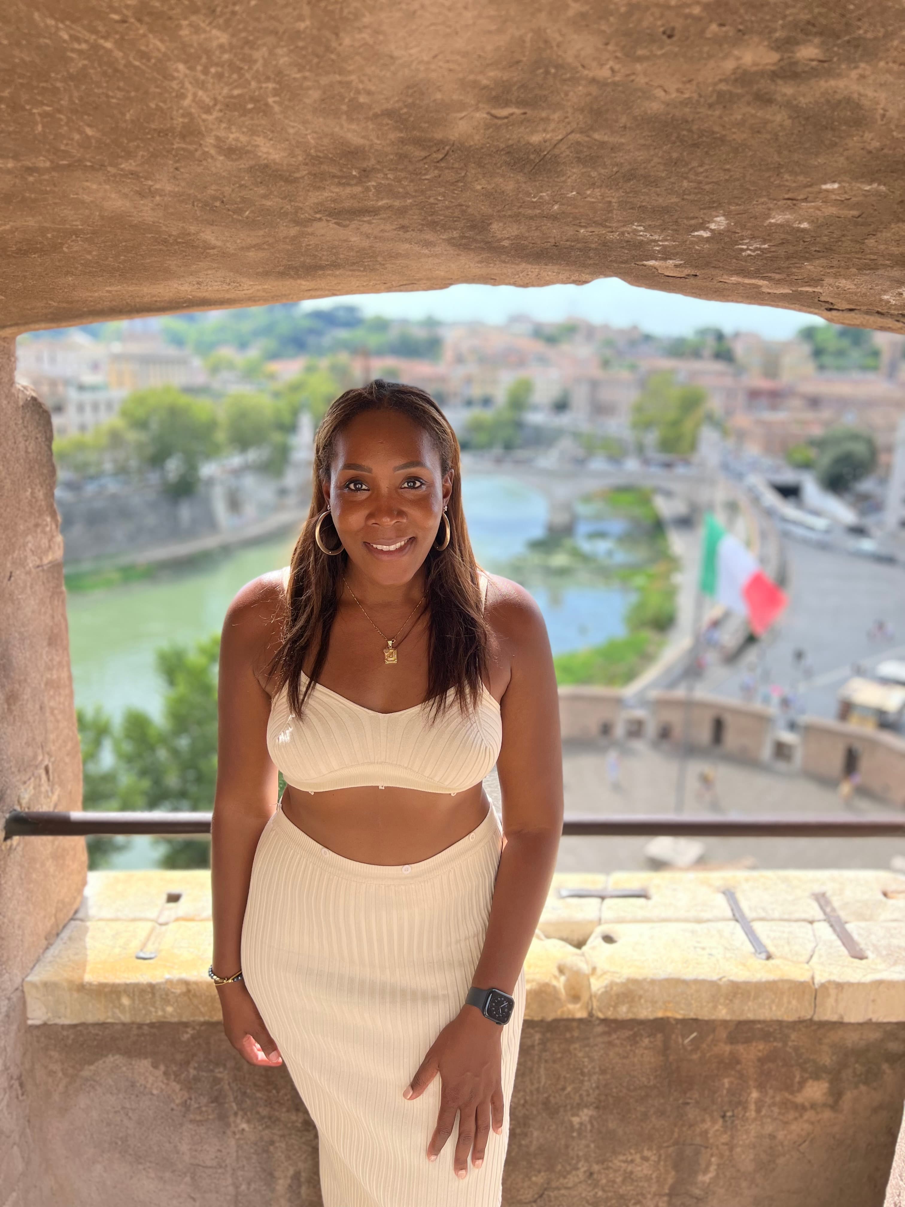 Jessica in a white outfit posing for a photo in a window with a beautiful city view behind her