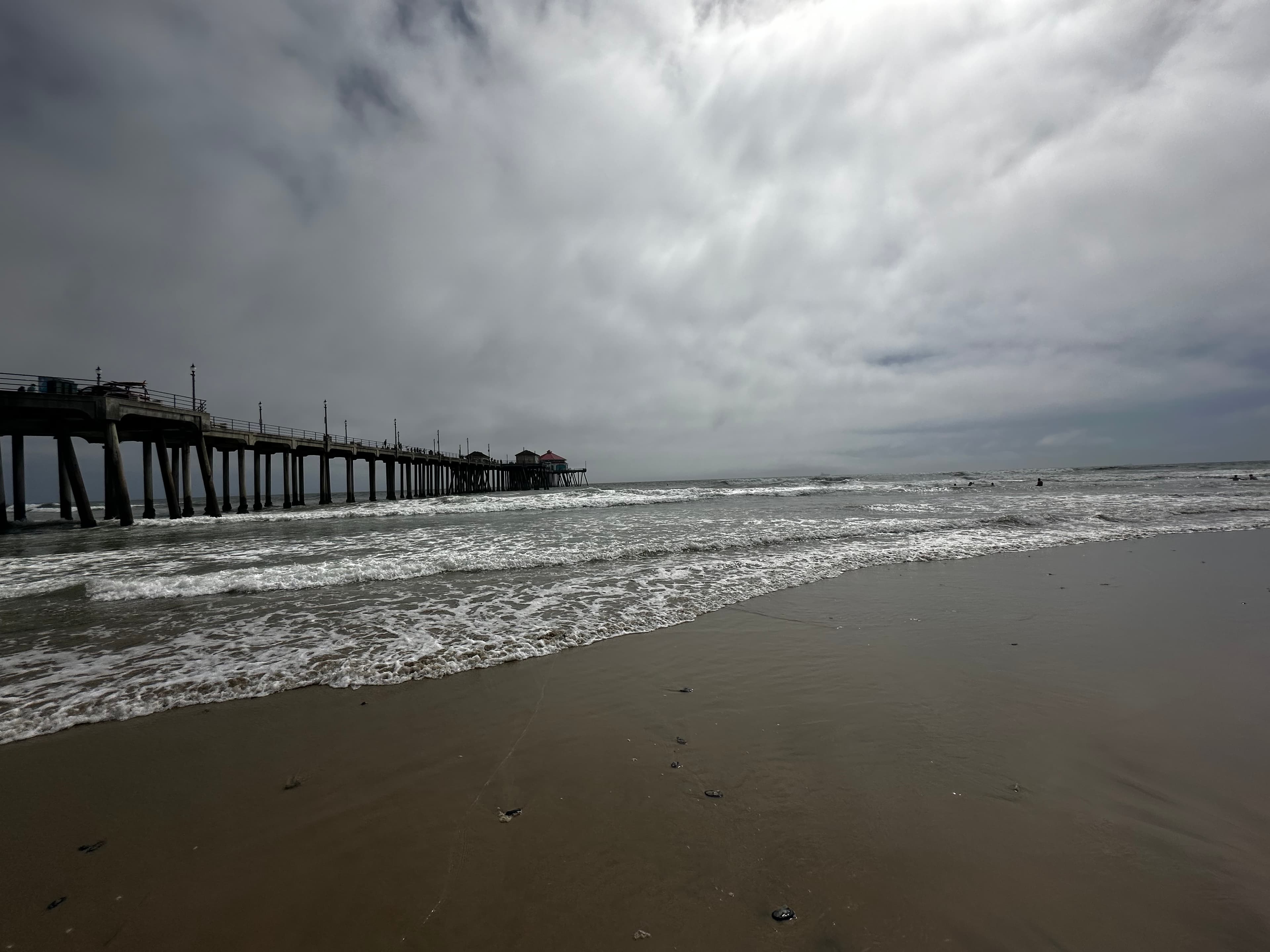 A pier jutting out into the ocean in the middle of a long beach on a cloudy day. 