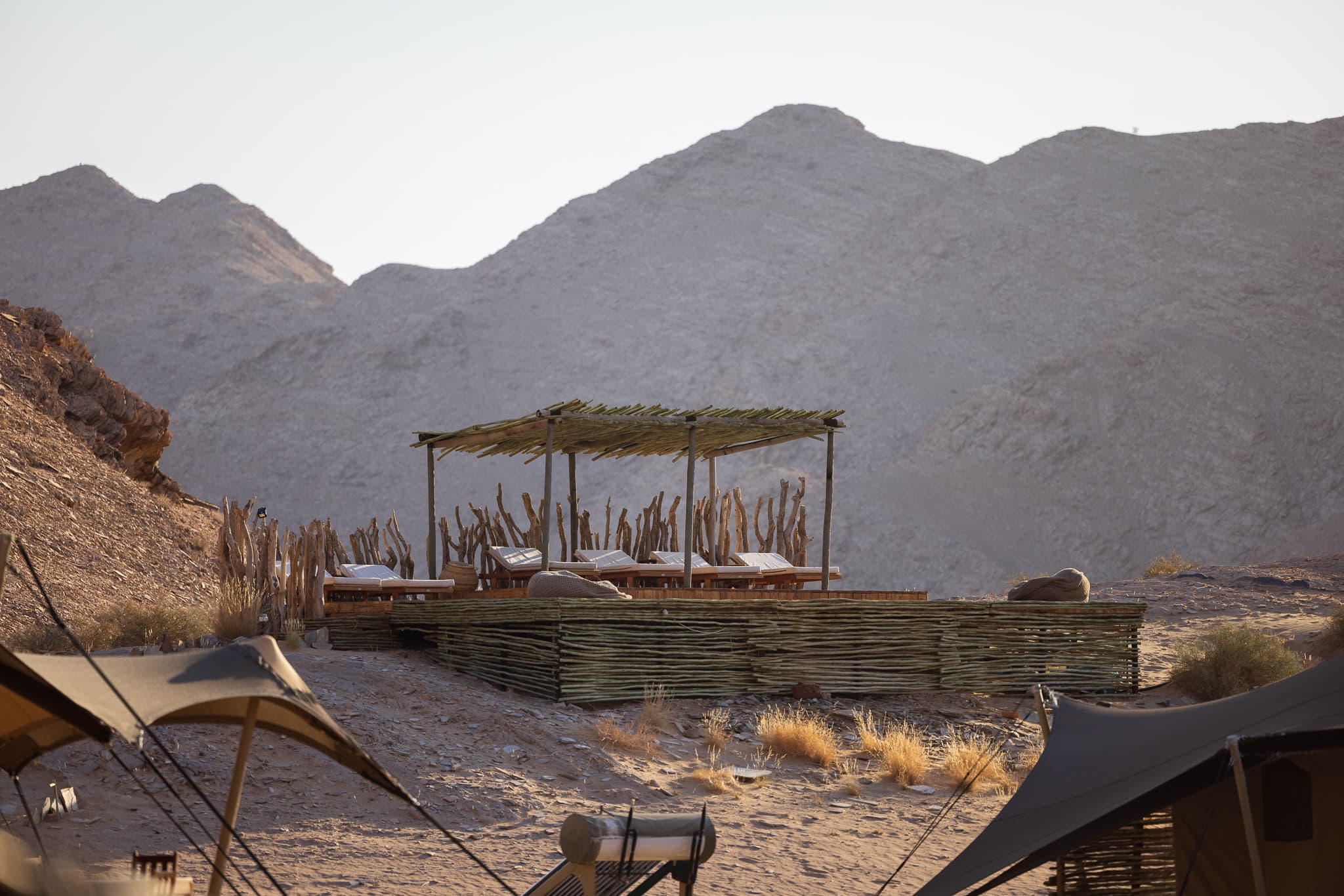 View of a wooden platform with lounge chairs and a thatched roof with a beautiful Mountain View in the background
