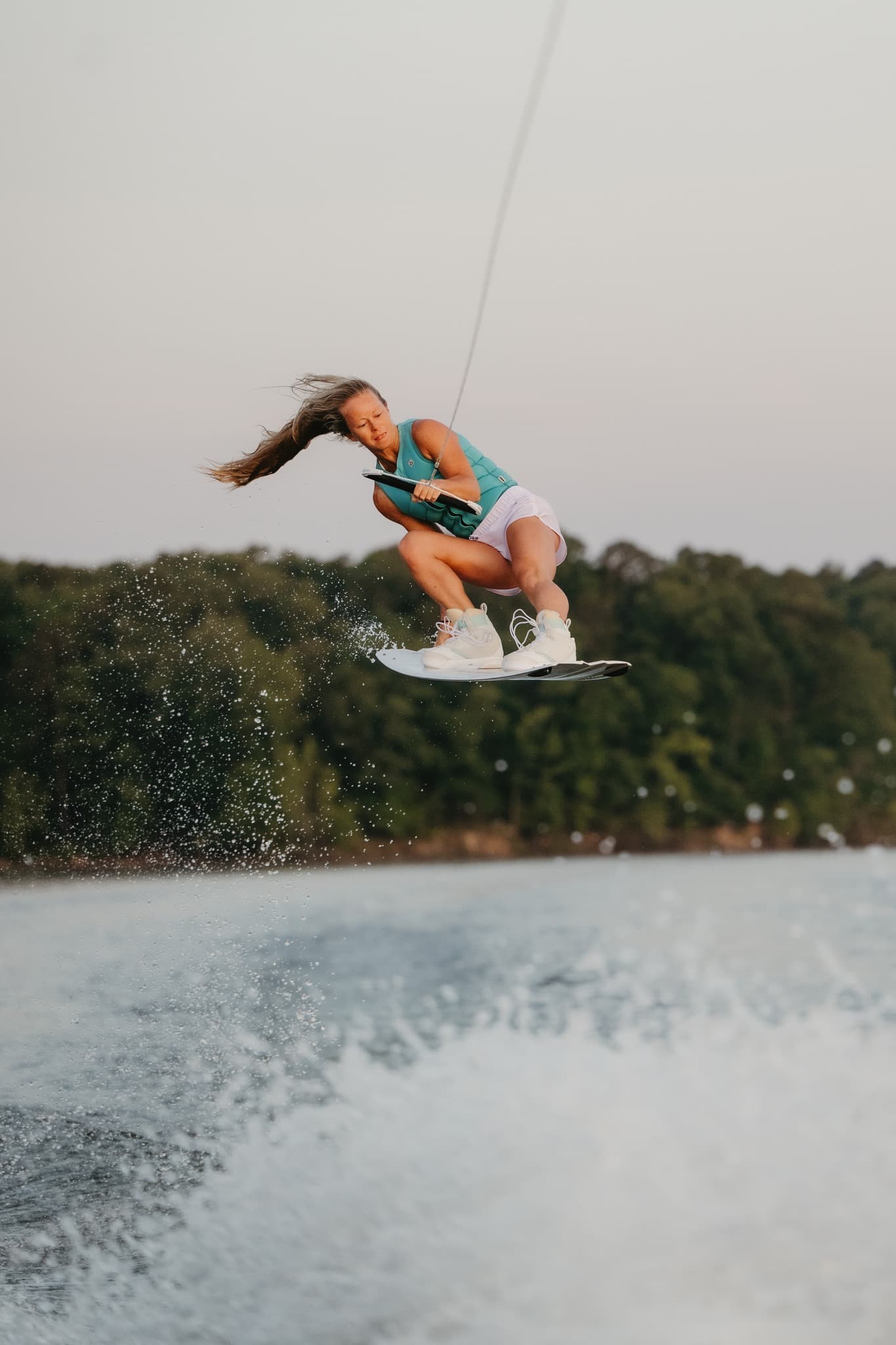 Maggie airborne while wakeboarding on a lake on a cloudy day