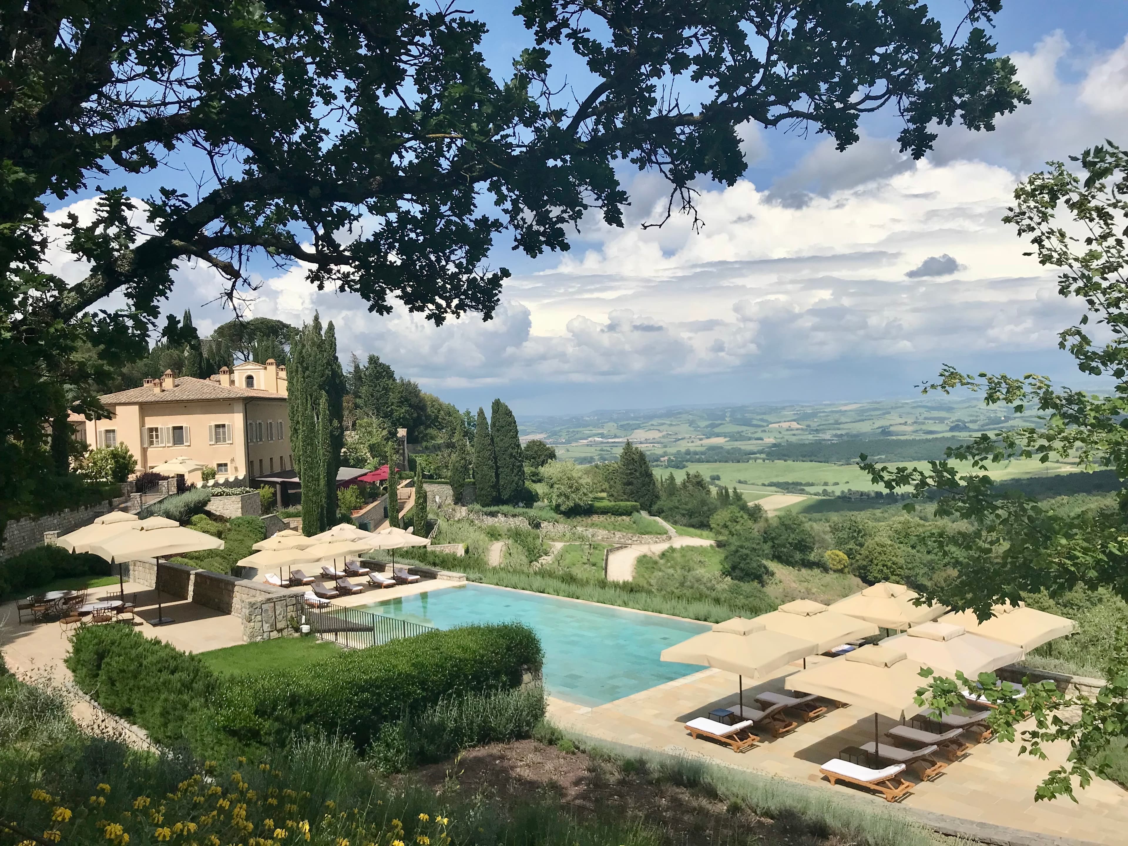 View of a beautiful hotel swimming pool and property surrounded by trees in the hills of Tuscany