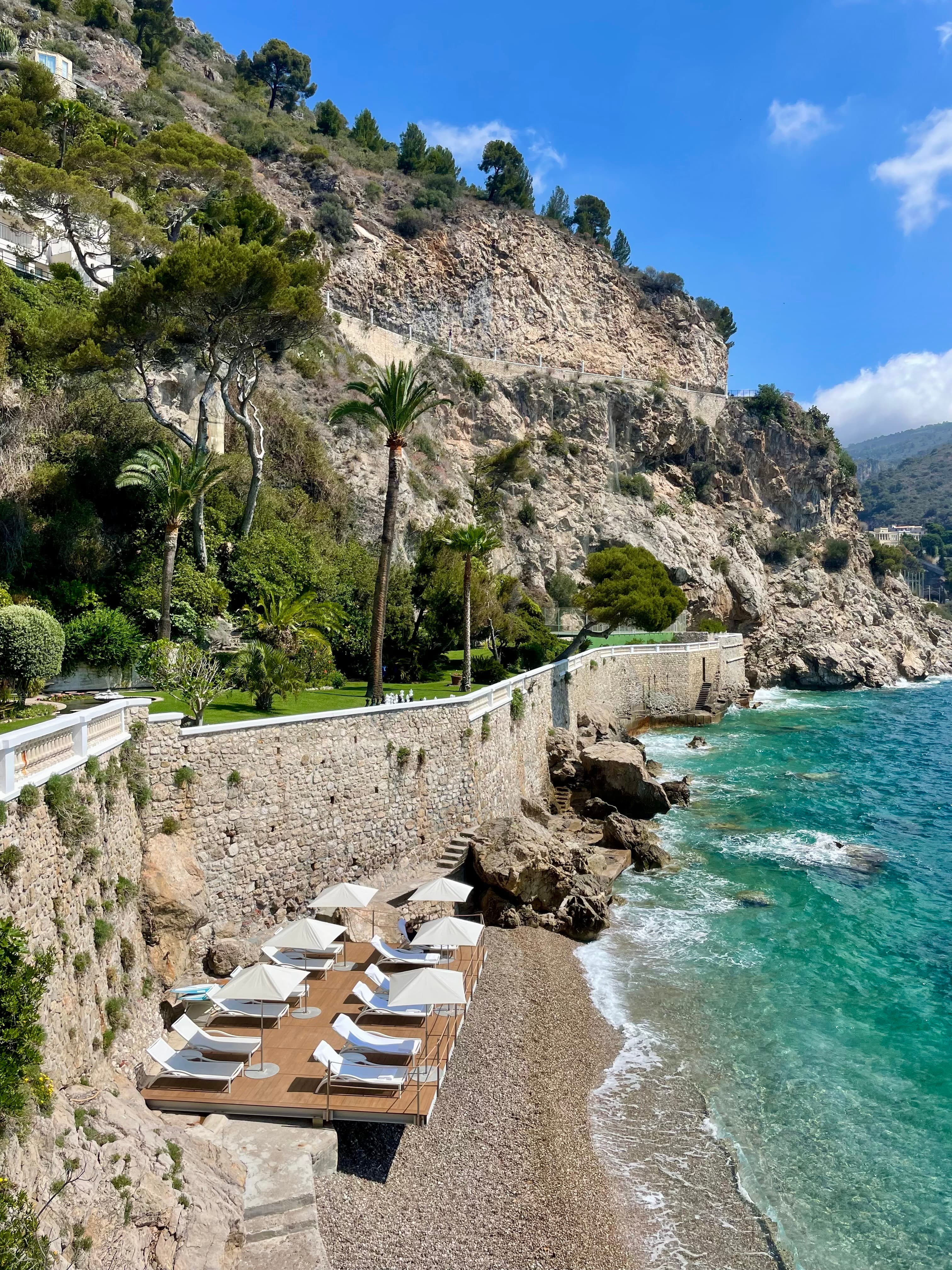 Beautiful view of blue sea and dramatic coastline with cliffs and lounge chairs visible on a rocky beach