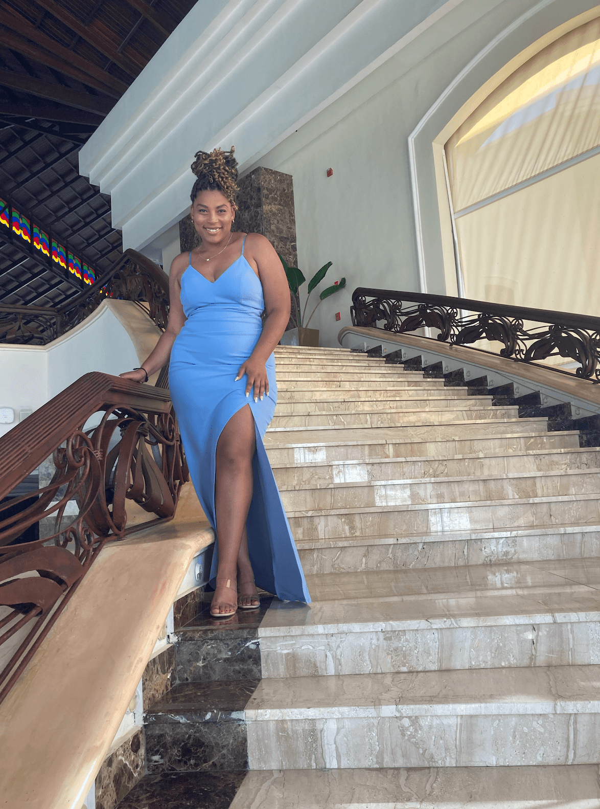 Advisor posing in a blue dress on a classic staircase with large windows. 