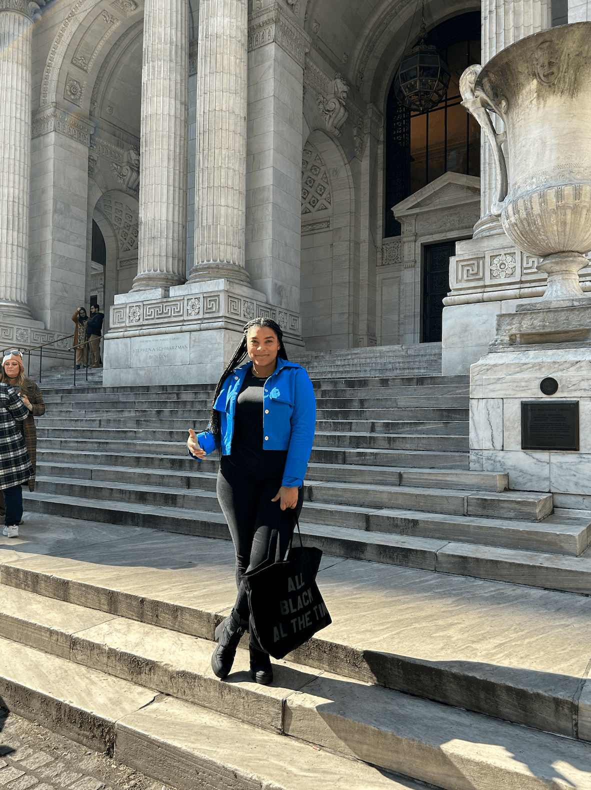 Advisor posing of an image in a blue coat on a sunny day with large steps and a building with pillars in the background. 