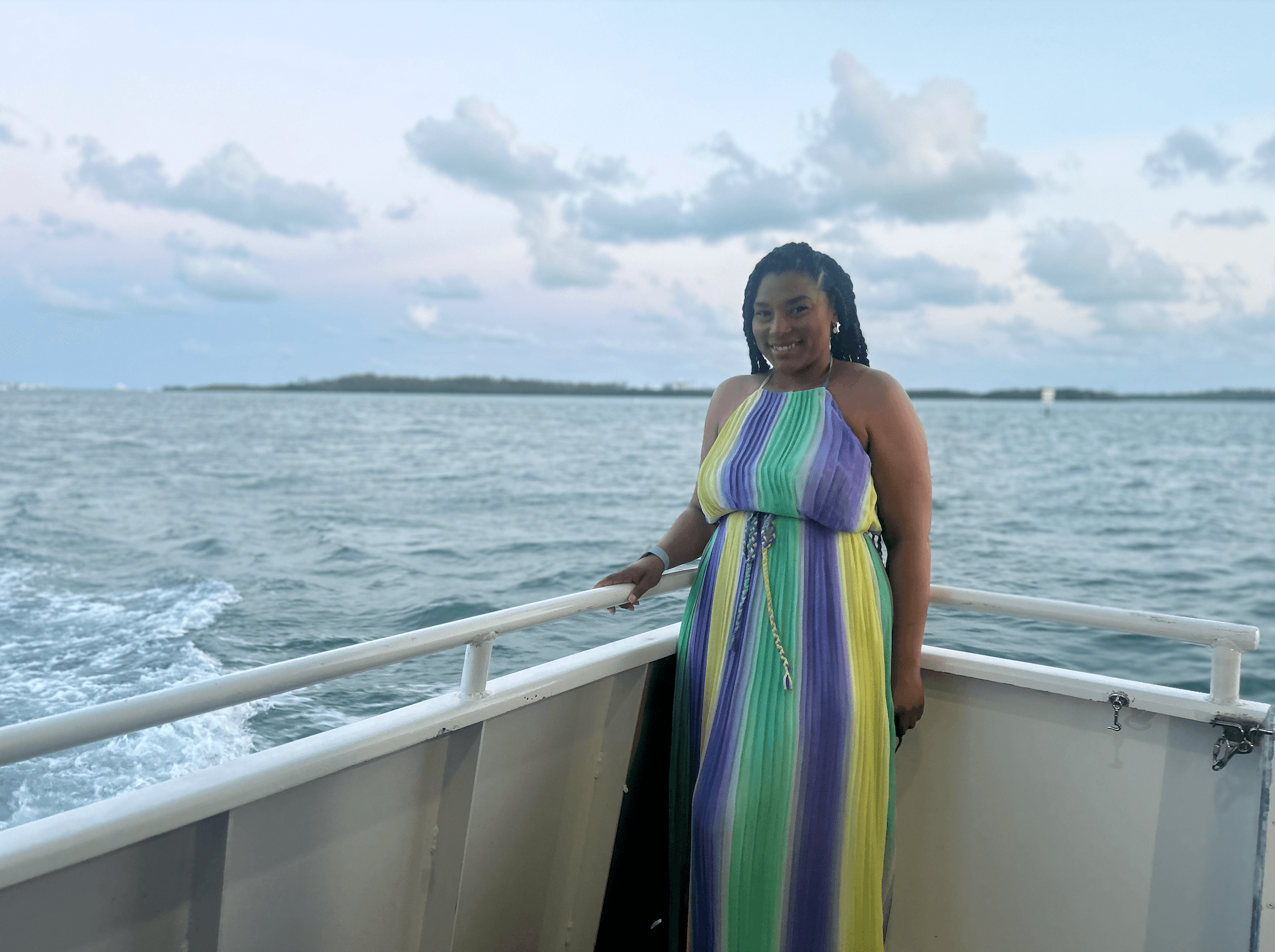 Advisor posing on the edge of a boat at dusk in a colorful dress and the ocean in the distance. 