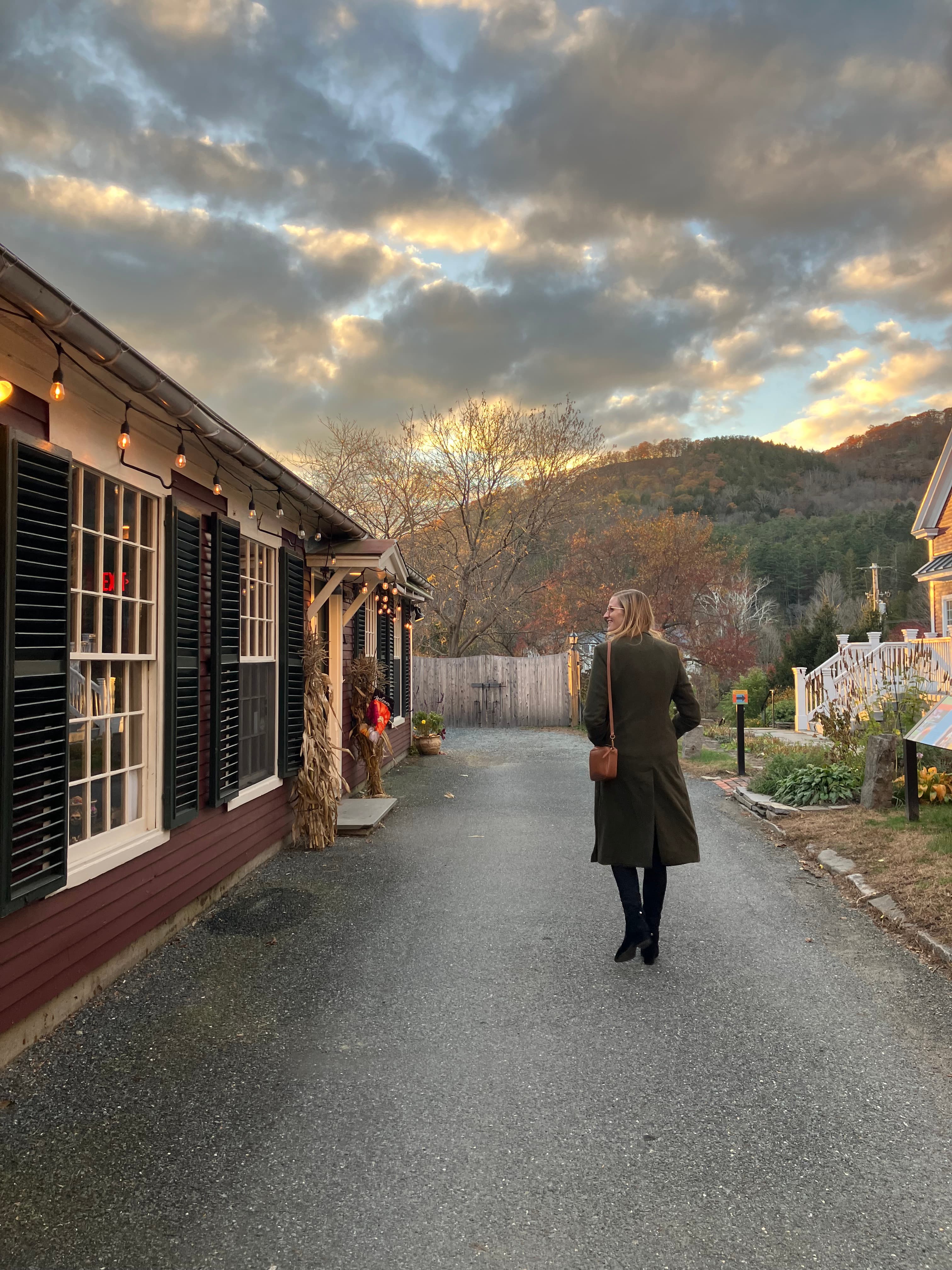 The advisor walking down a secluded path with a quaint building on the side with a mountain scape and foliage in the distance at dusk.
