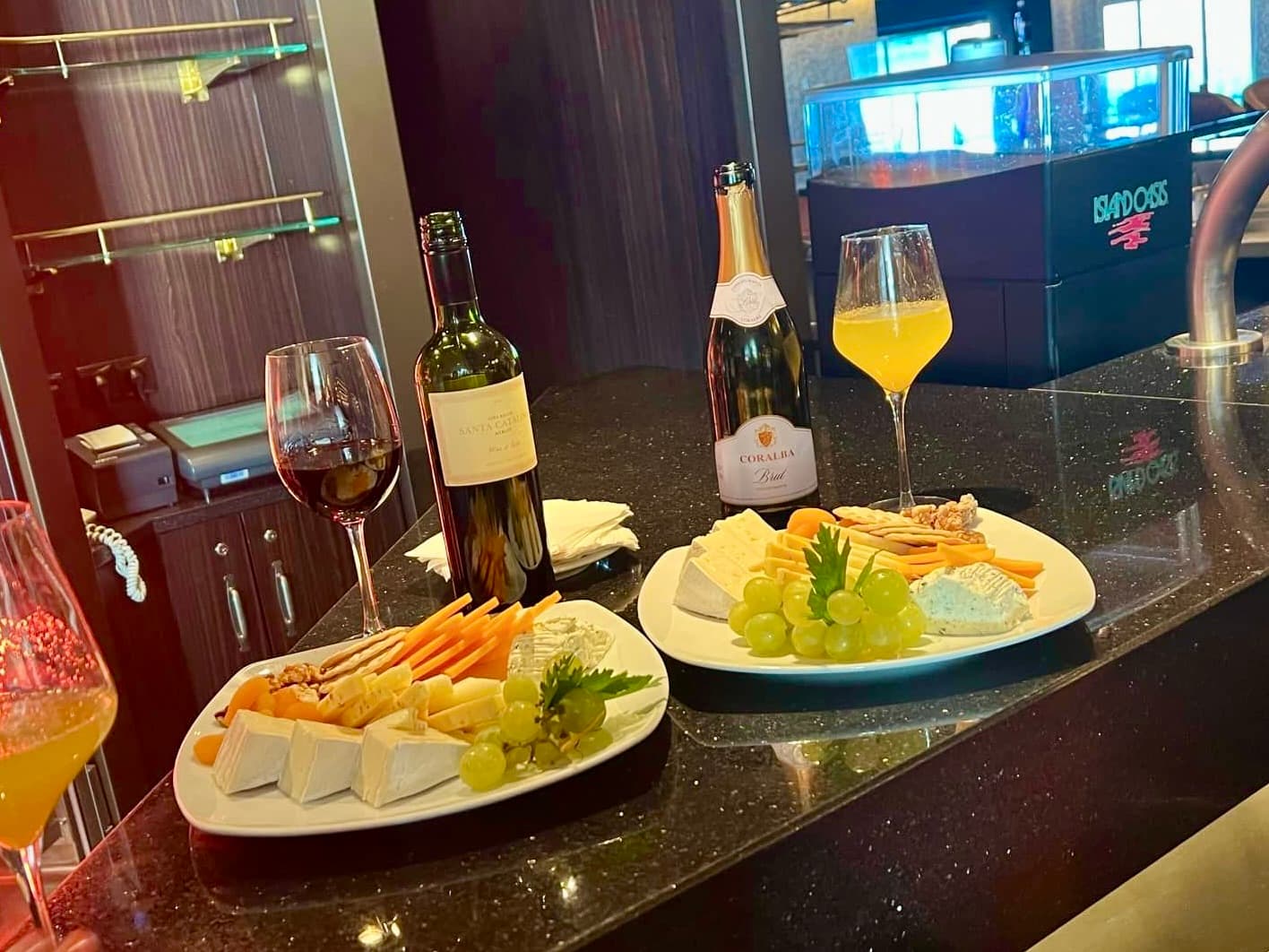 Two glasses of wine and dinner plates on a dark wood bar setting.