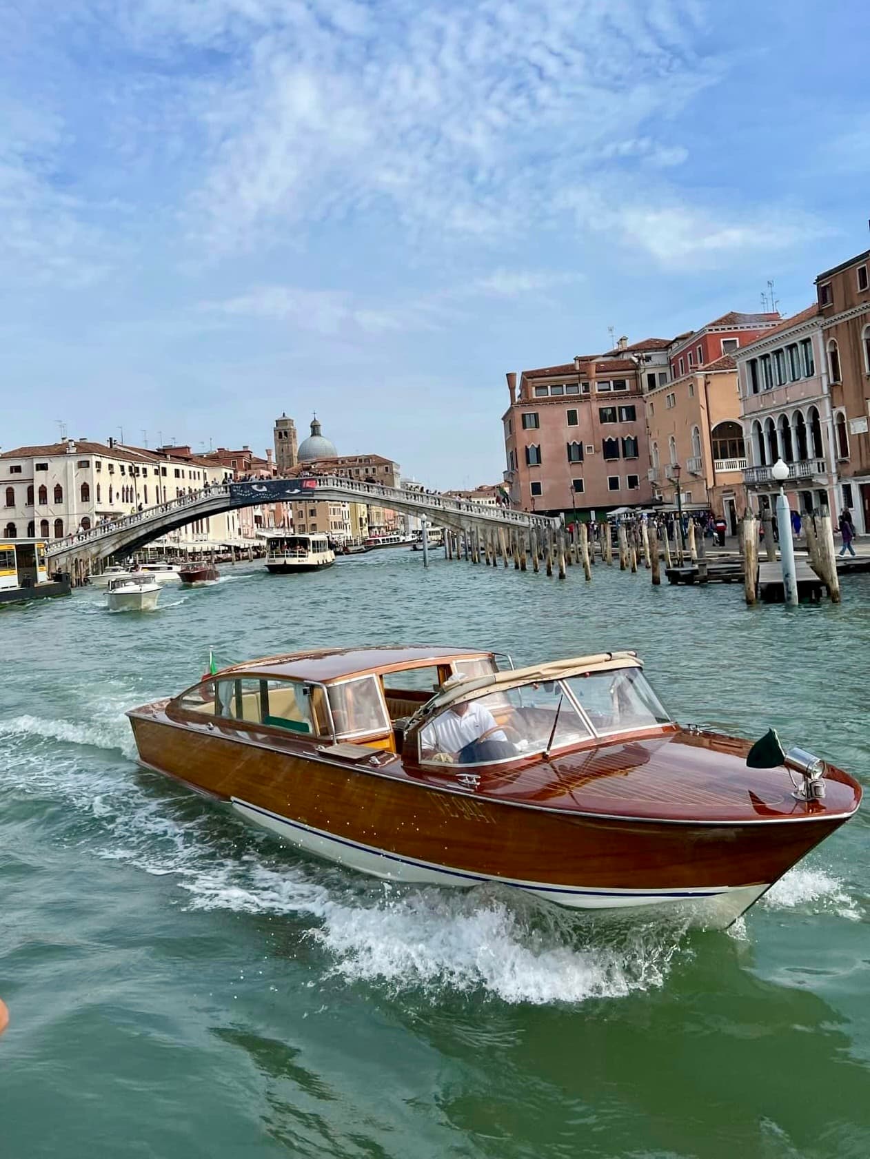 A midsize fishing boat cruising beneath a bridge in front of historical buildings.
