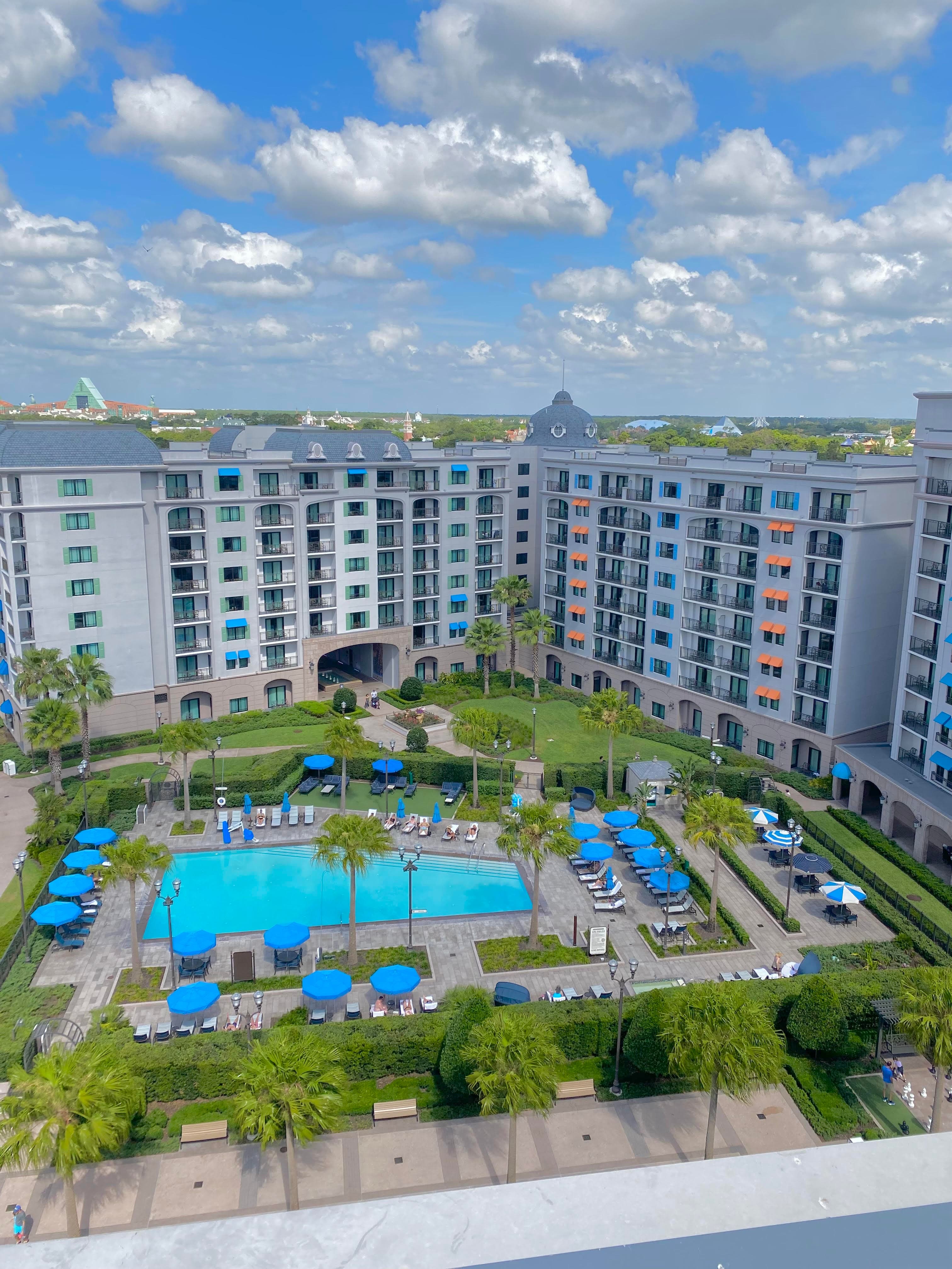 A view of a beautiful resort with a large pool, loungers with sun umbrellas and foliage on a sunny day. 