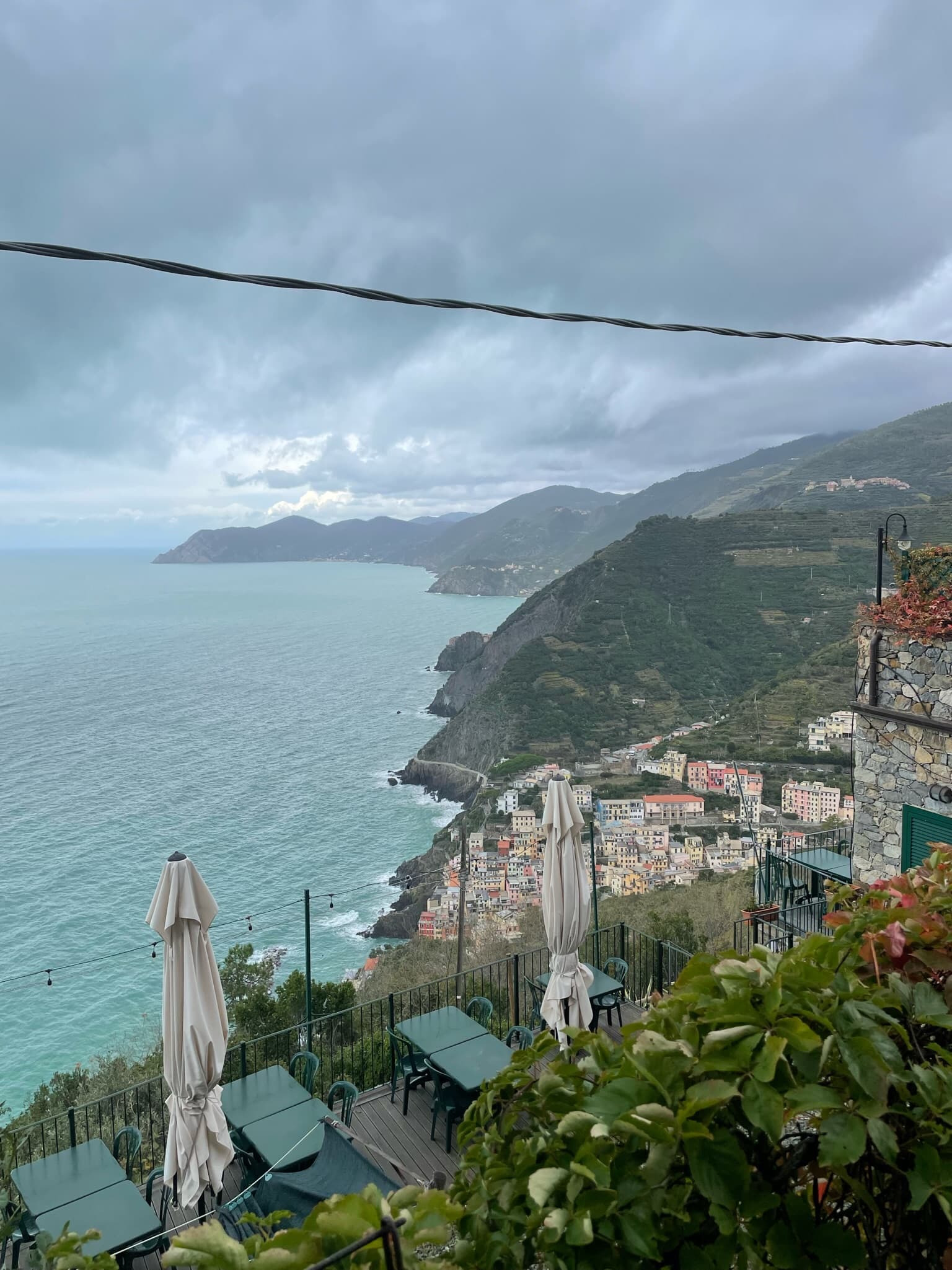 A coastline view from the hills depicting cliffside dwellings from an open patio on a cloudy day. 