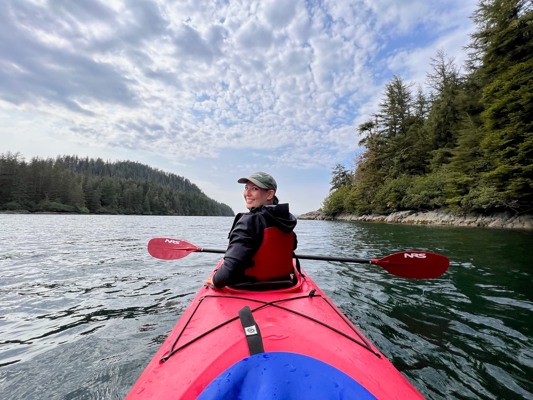 A person in a red kayak floating on a calm body of water during the day.