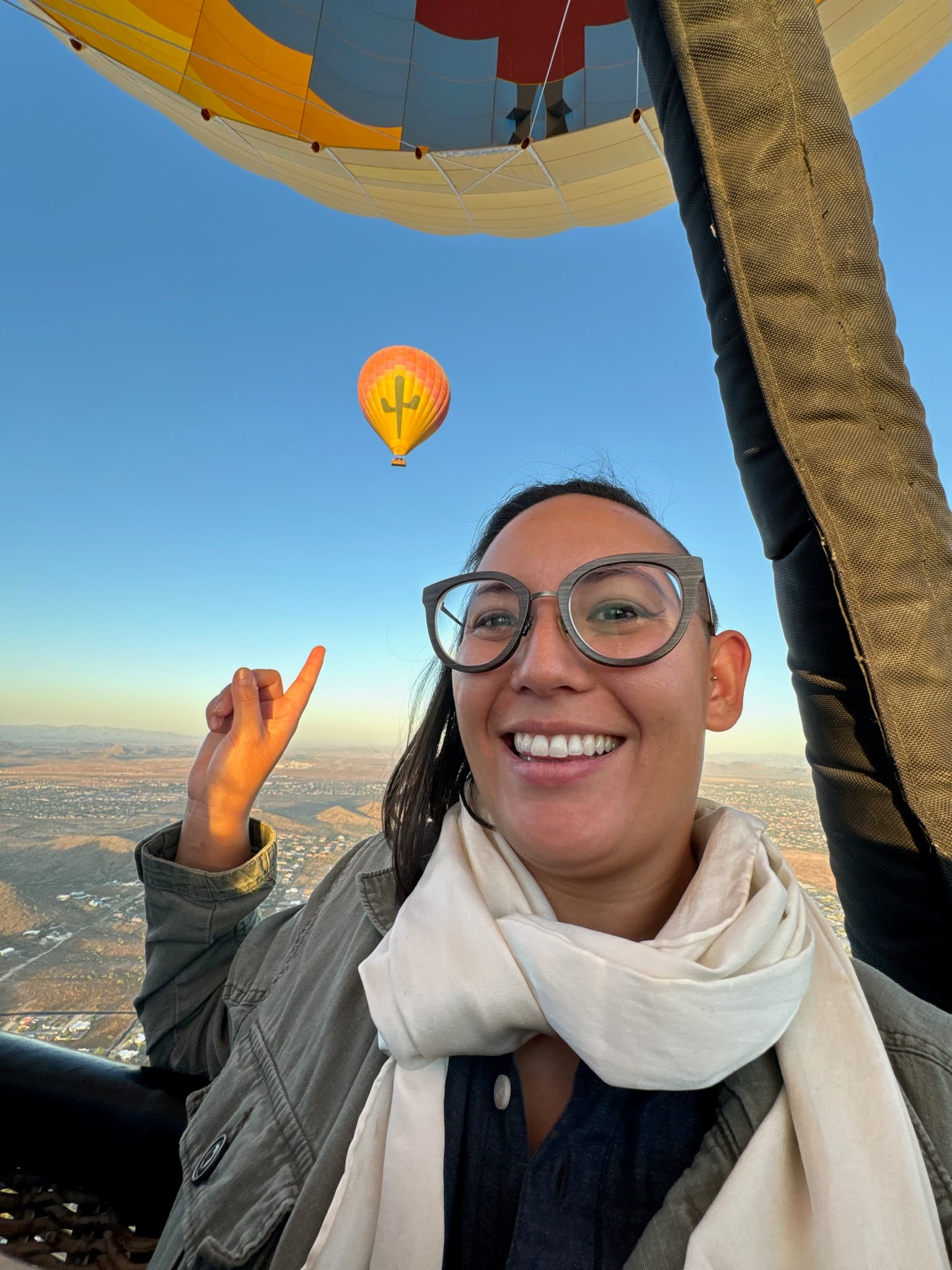 A person flying in a hot air balloon pointing at another hot air ballon behind them high in the sky.