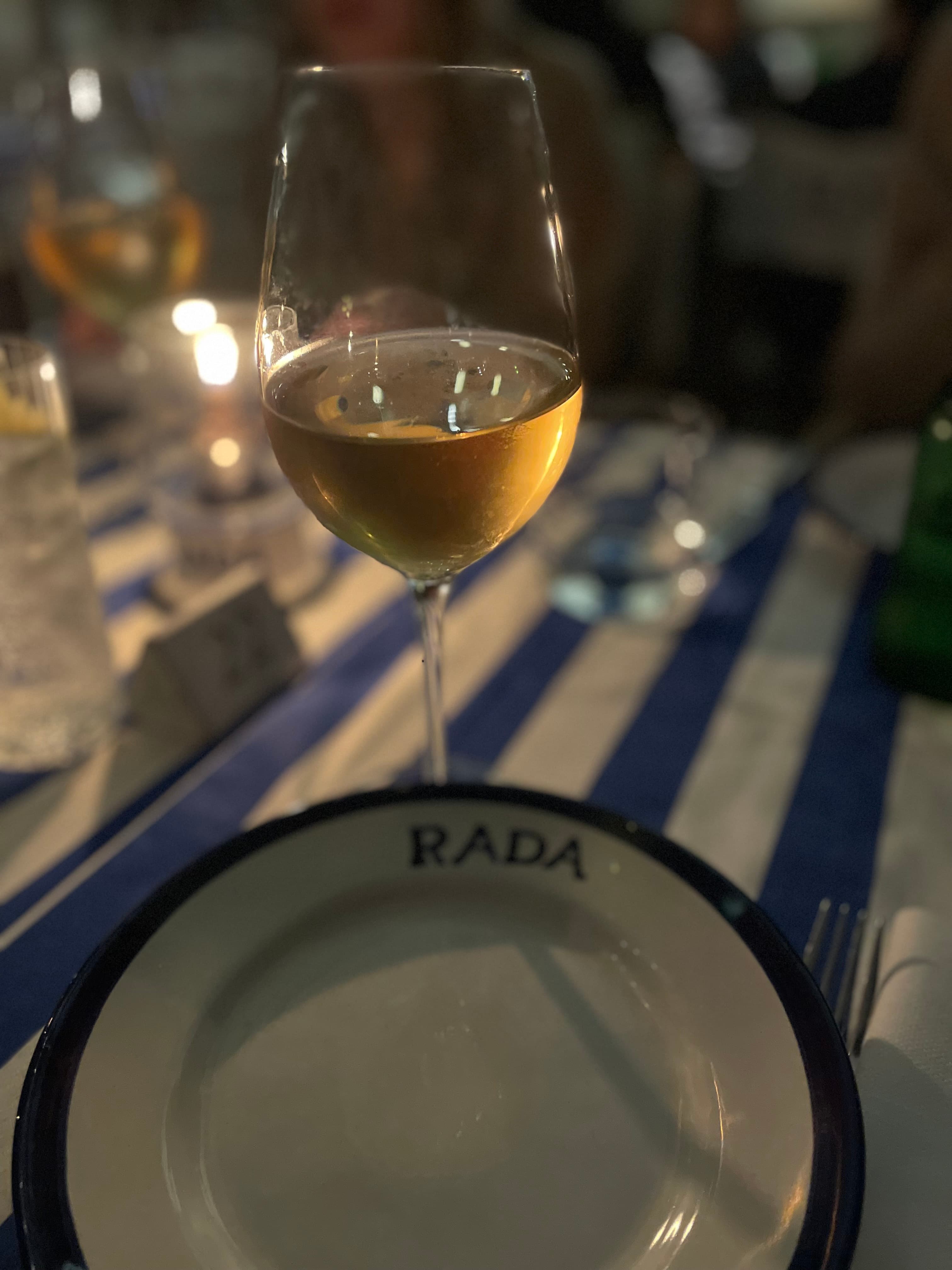 View of a glass of white wine and small plate on a striped table in a darkly lit room