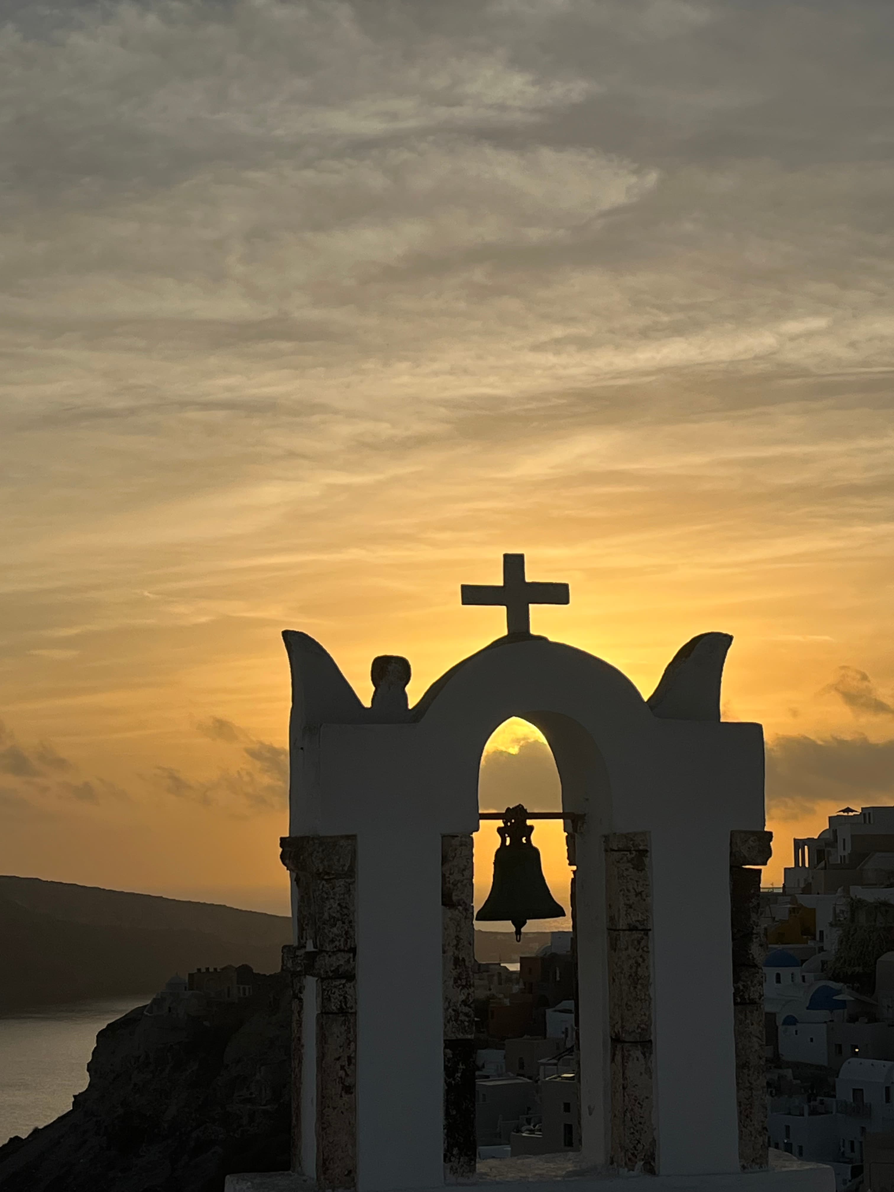 Image of a church bell outdoors with a sunset in the background.