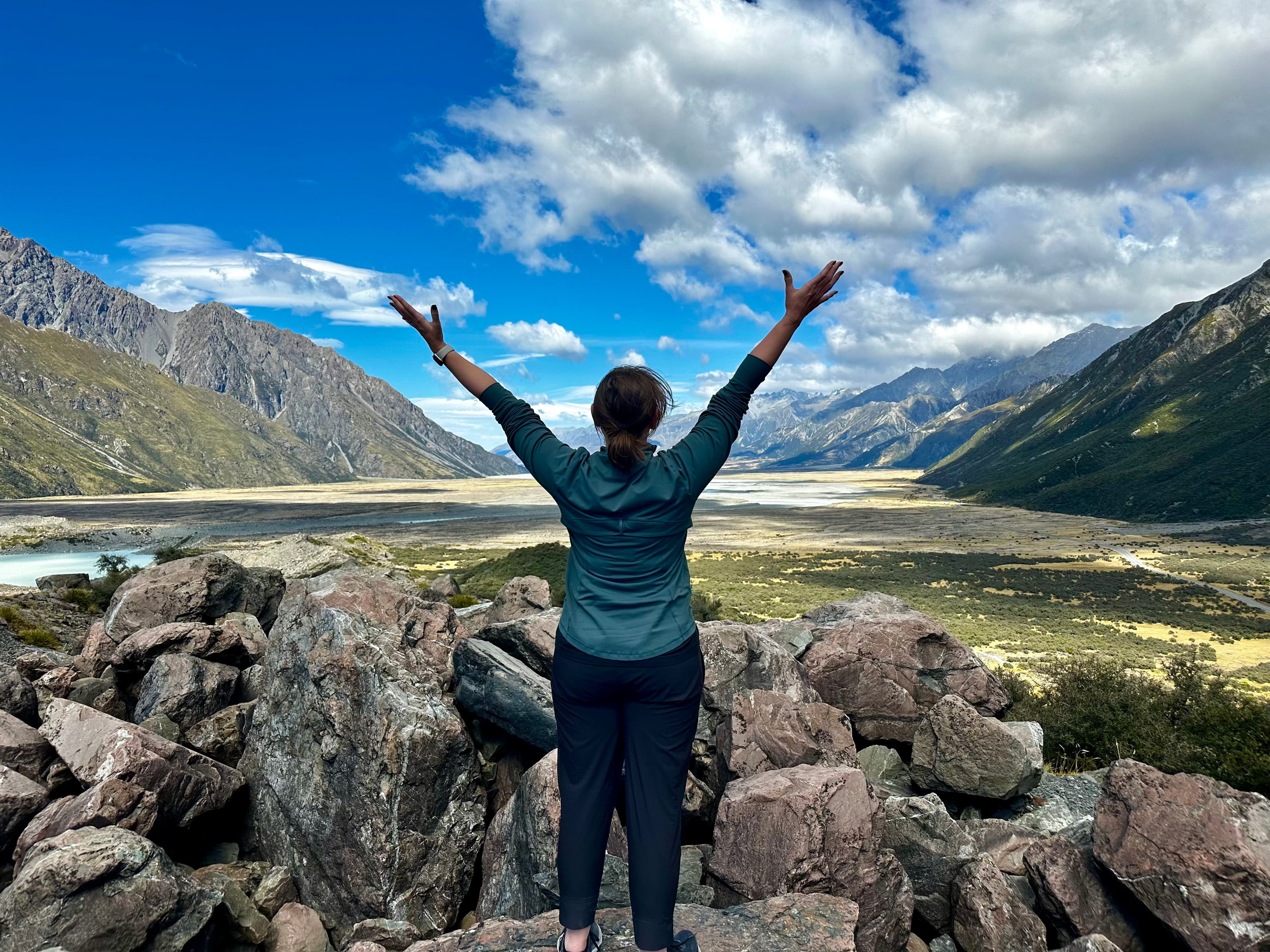 Advisor posing with arms outstretched to the sky, looking towards the mountains in the distance.