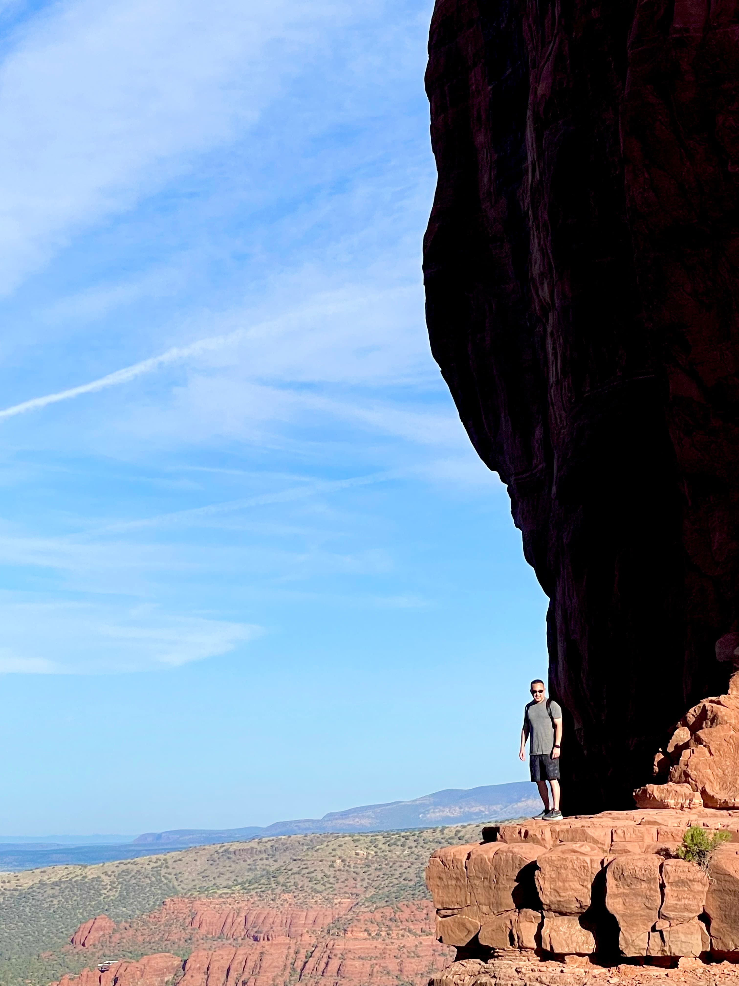 Scott standing on the edge of a red rock cliff with an expansive valley view behind him on a clear day