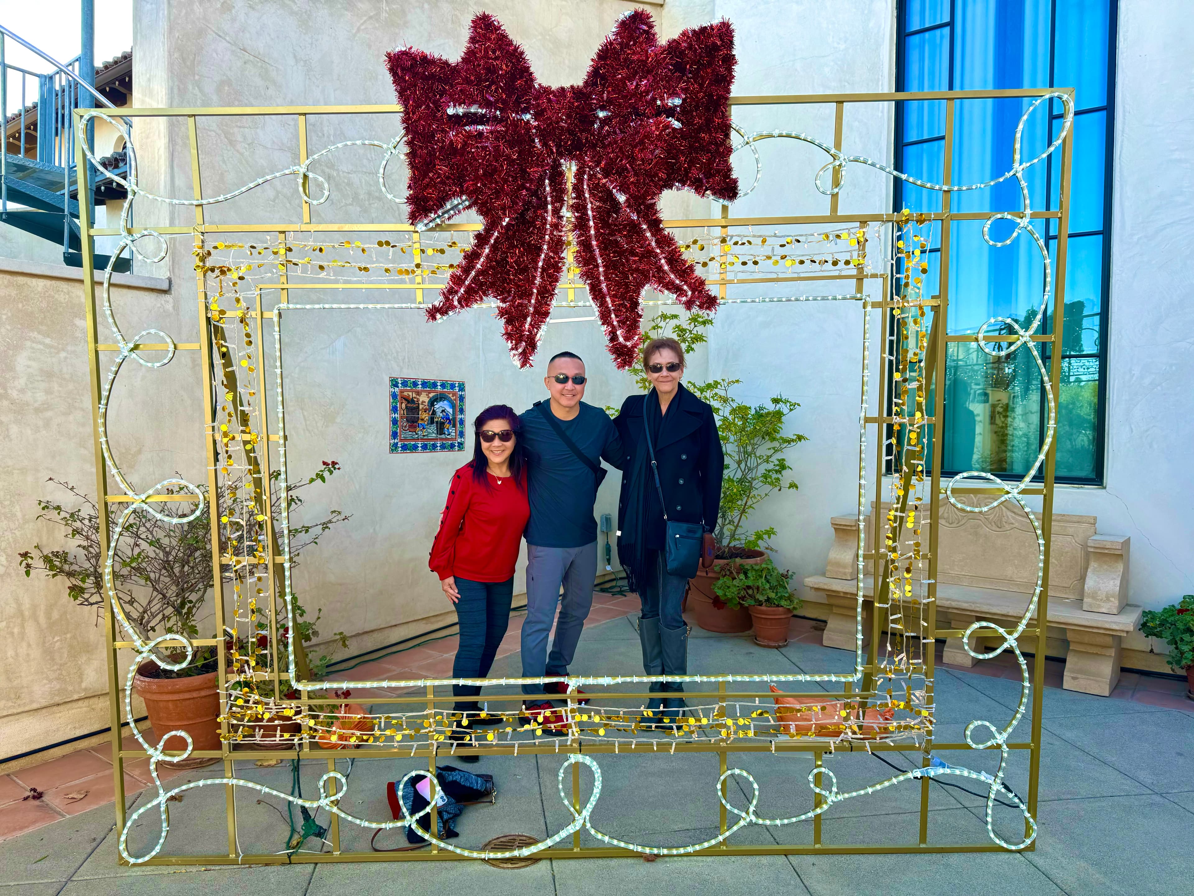 Scott and two others with their arms around each other posing behind a lit up frame in the shape of a present