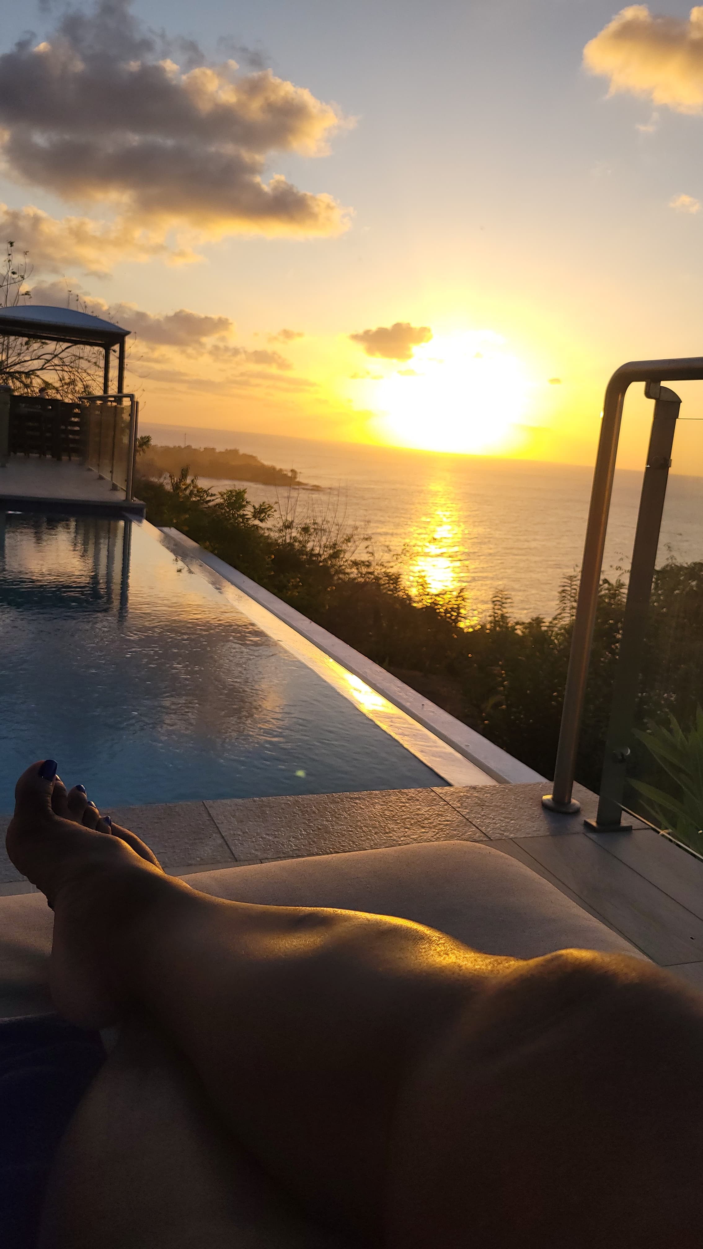 A view from someone sitting at a pool overlooking a calm ocean at sunset.