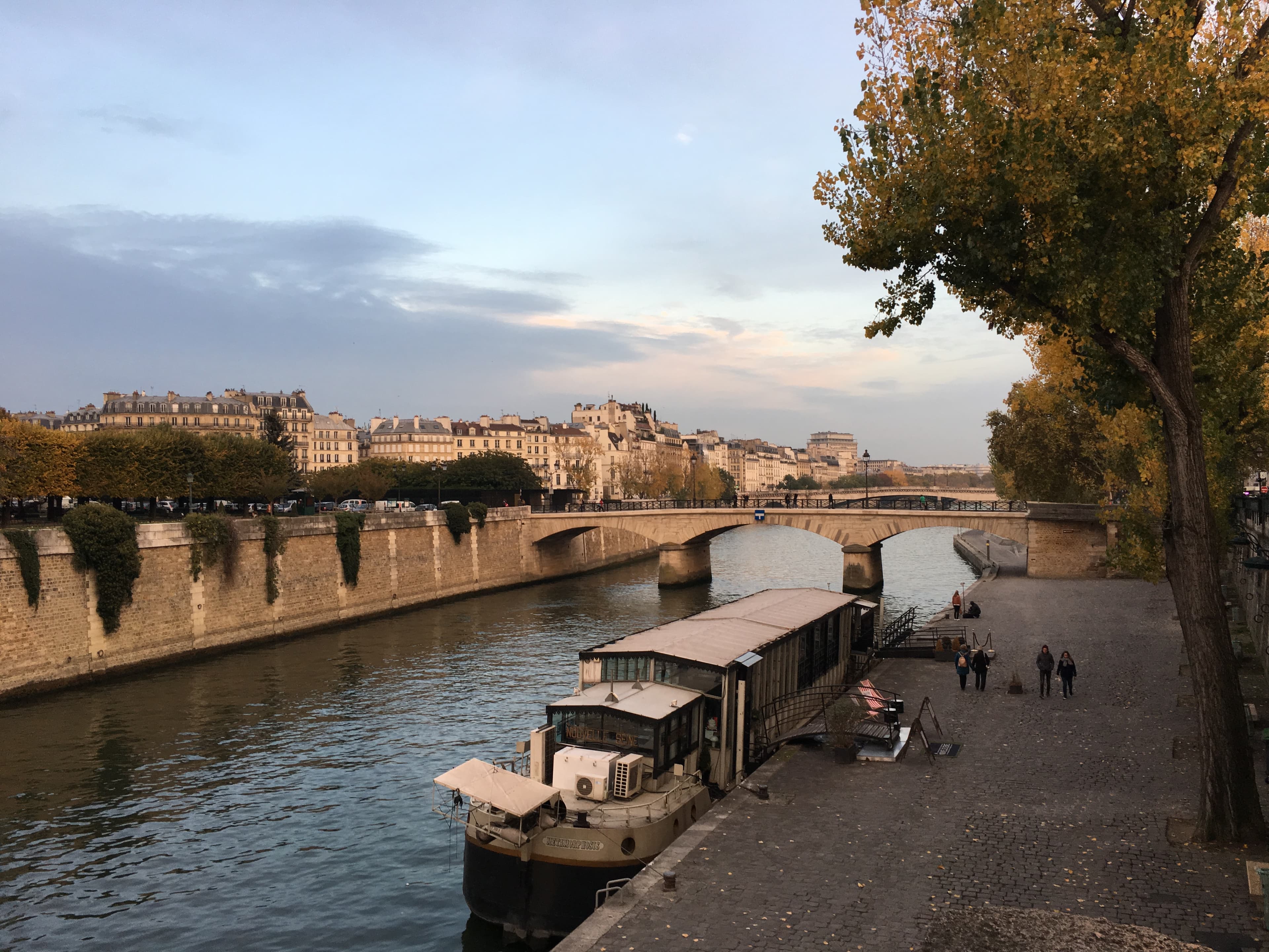 Beautiful view of a river with a large boat docked and a stone bridge connecting either side on a sunny day