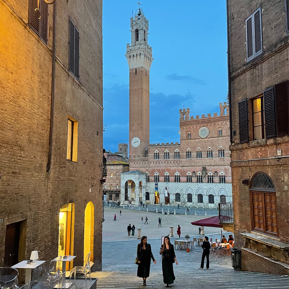 View of a beautiful plaza with several pedestrians and a large clock tower in Siena, Italy at dusk