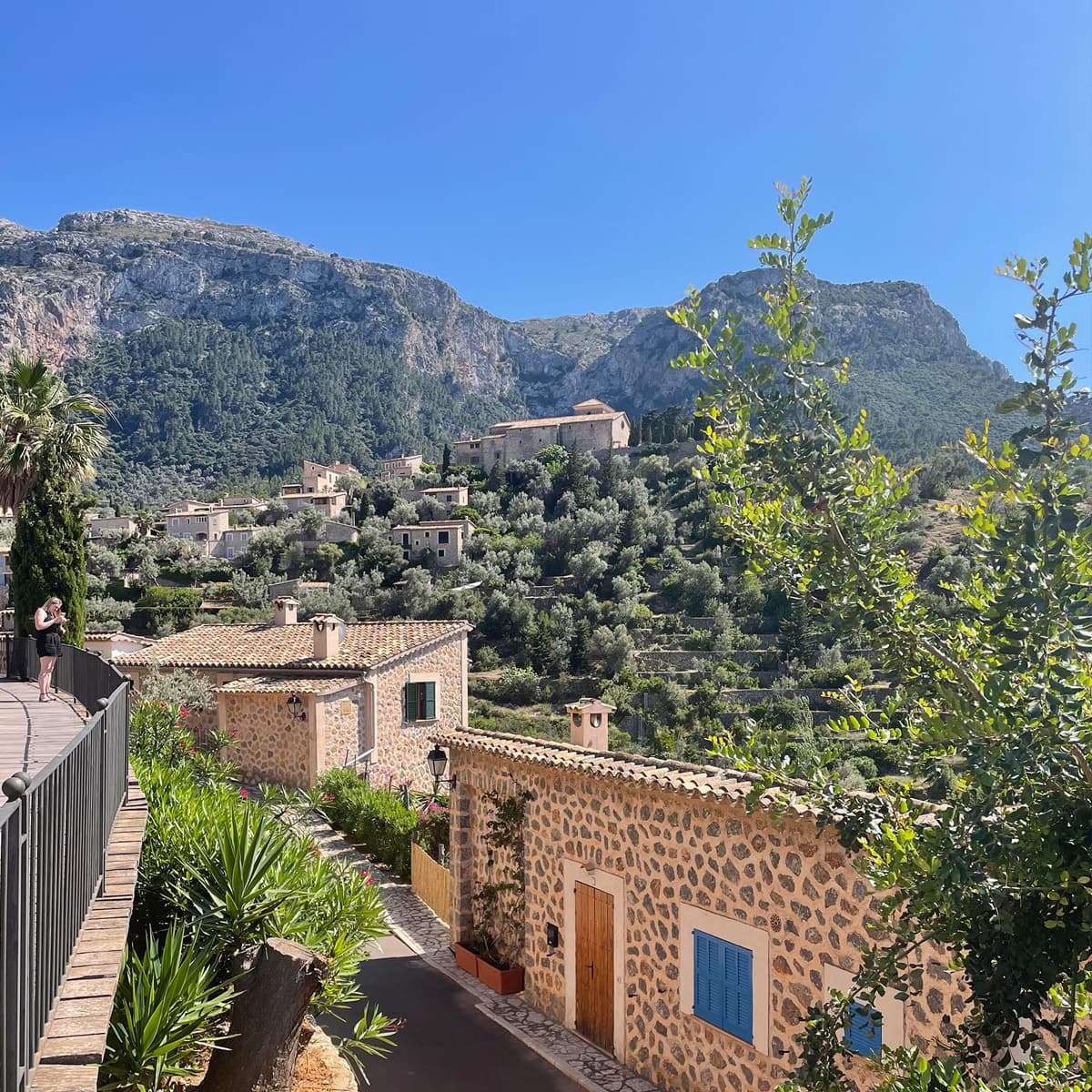 Pretty view of stone buildings on a green hillside with many plants and trees under sunny skies