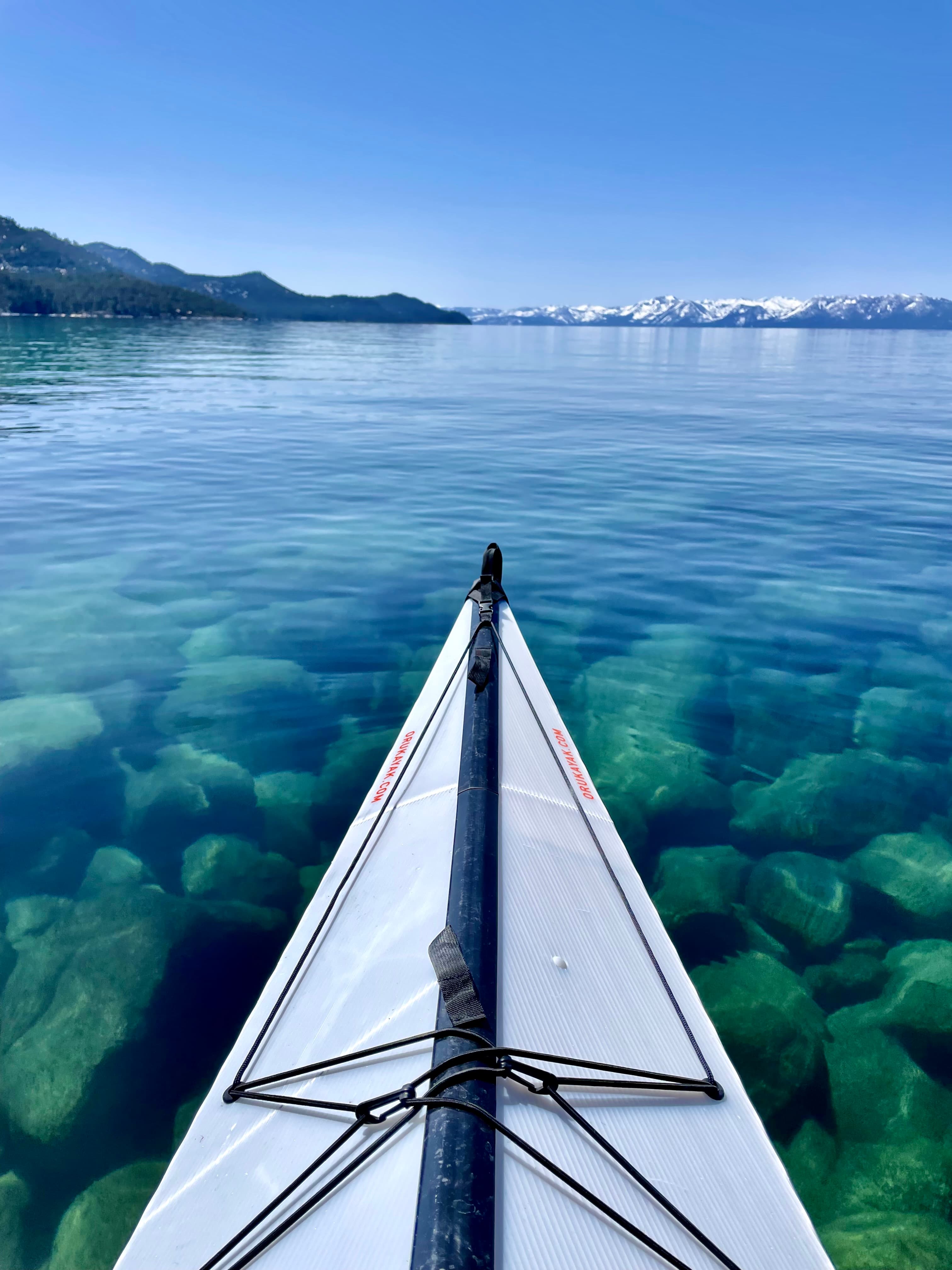 View of the front of a boat over crystal clear waters with snowy mountains visible on the horizon under clear skies