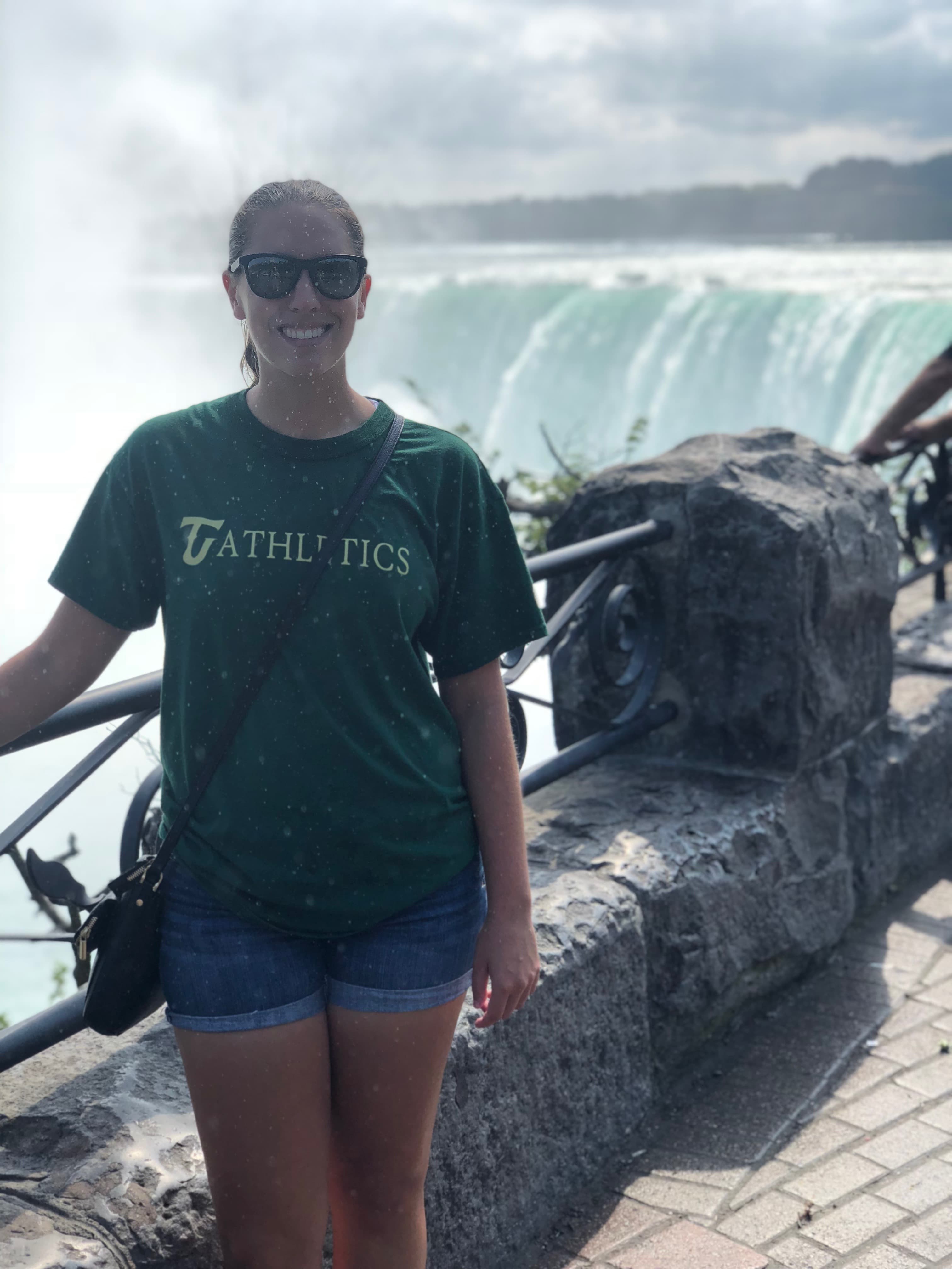 Advisor wearing a green t-shirt and standing in front of a waterfall.
