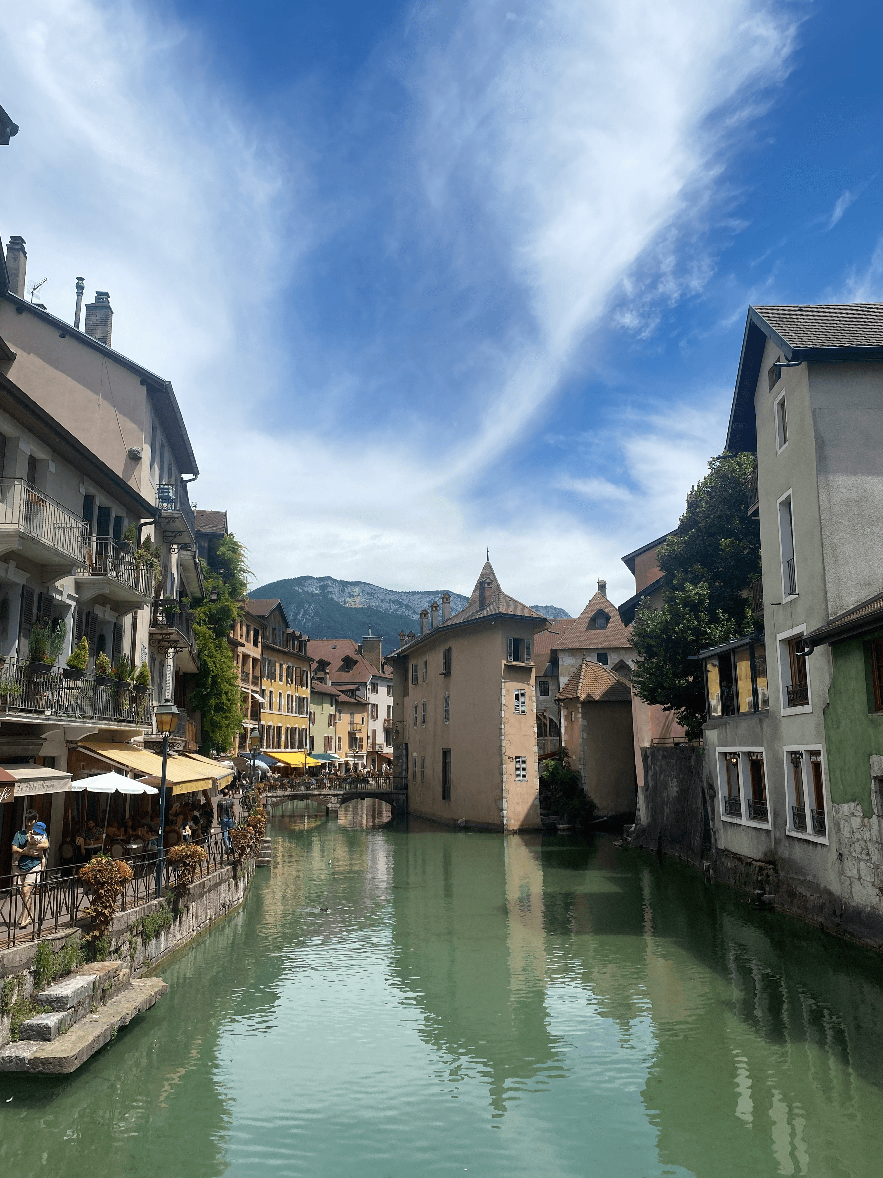 A beautiful view of a river in between old buildings leading up to mountains in the distance on a sunny day