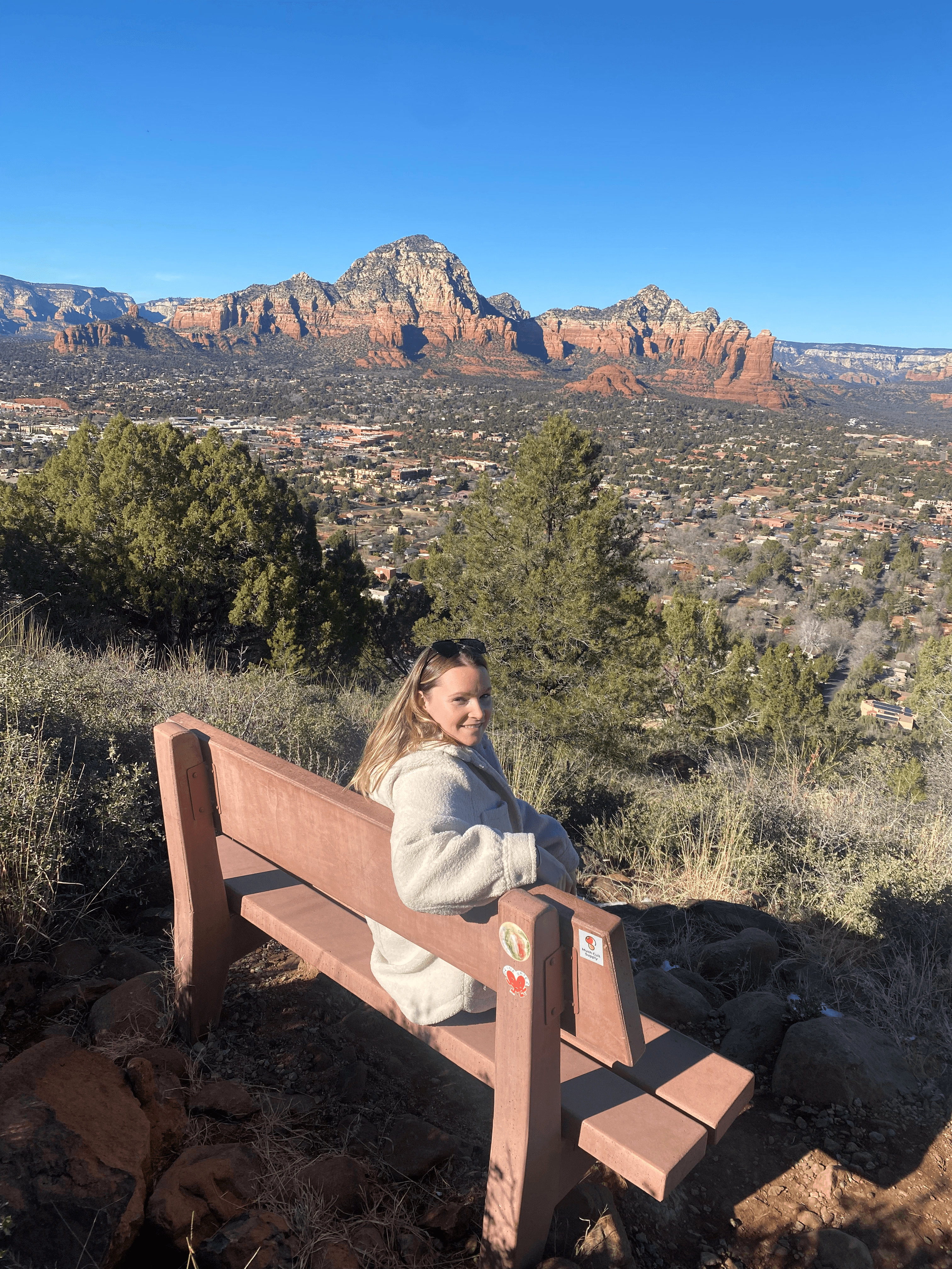 Eliana sitting on a bench overlooking a beautiful valley with mountains in the distance under clear skies